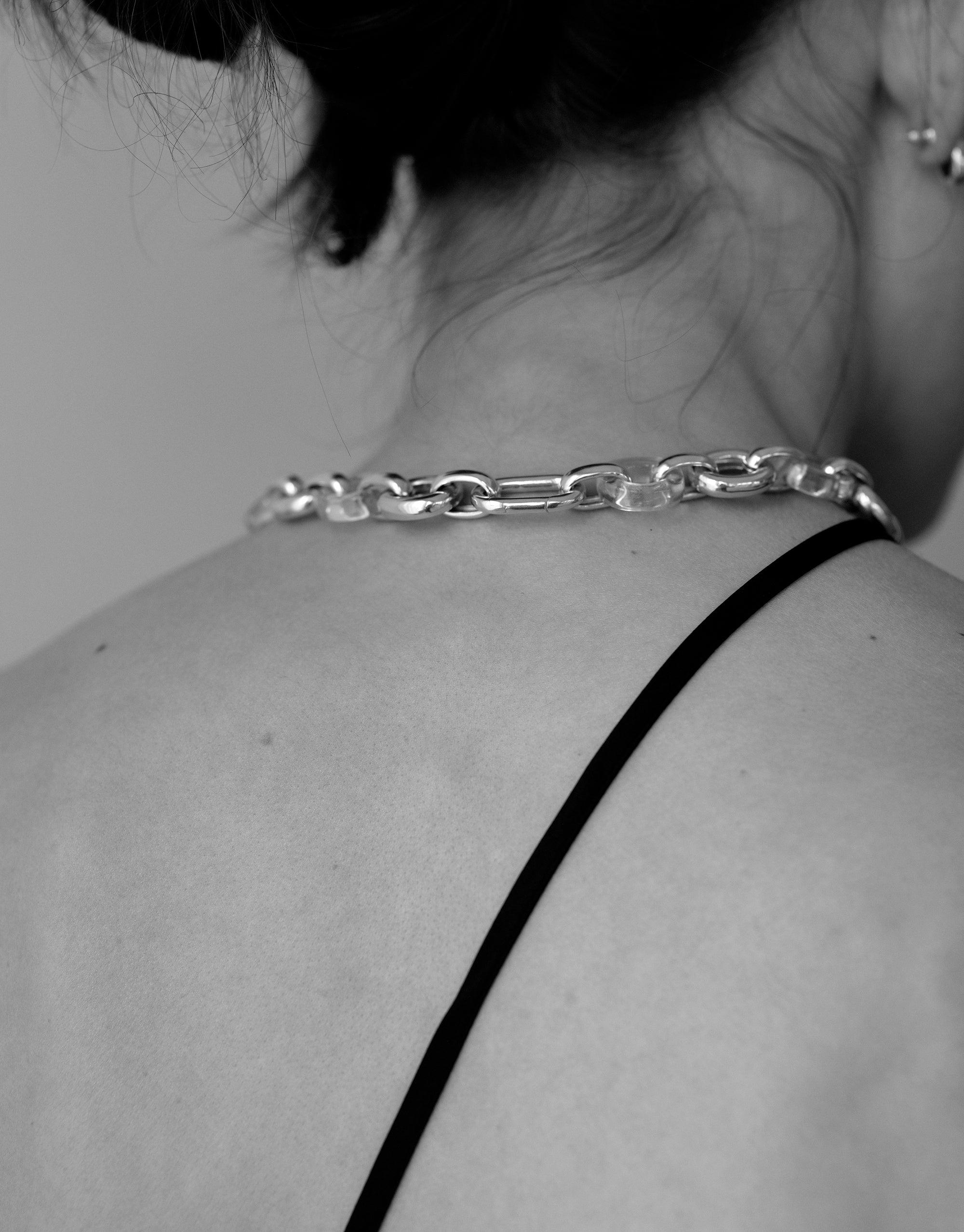 Close-up of a person's shoulder wearing the Connected Loop Necklace, showcasing its mixed metal chain design. The necklace rests elegantly on the skin, symbolizing unity and sustainability. Connected Loop Necklace | Mixed Metal & Glass by CLED.
