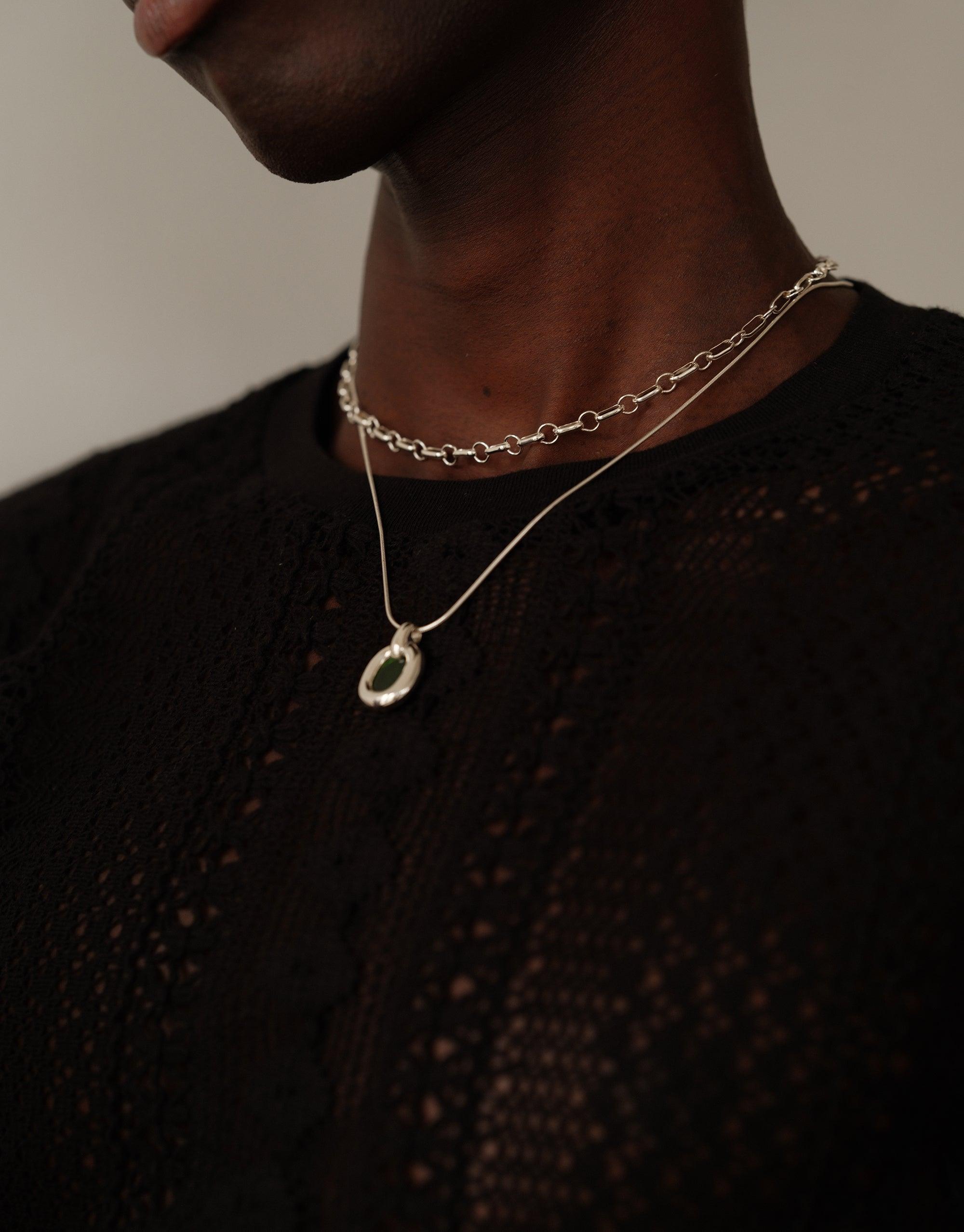 Close-up of a silver Core Loop Necklace with Snake Chain worn on a dark-skinned neck against a black textured top, showcasing the delicate pendant and layered chain design. Upcycled jewelry symbolizing unity and connection. Core Loop Necklace | Snake Chain by CLED.