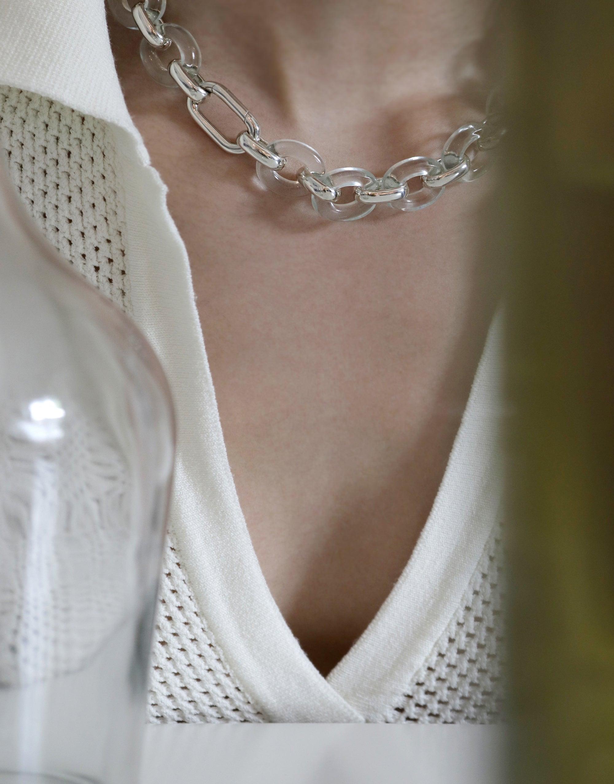 Elegant Connected Loop Necklace in clear glass, showcasing interlocking circular links. Worn against a white v-neck sweater, symbolizing unity and sustainability. Connected Loop Necklace | Glass by CLED