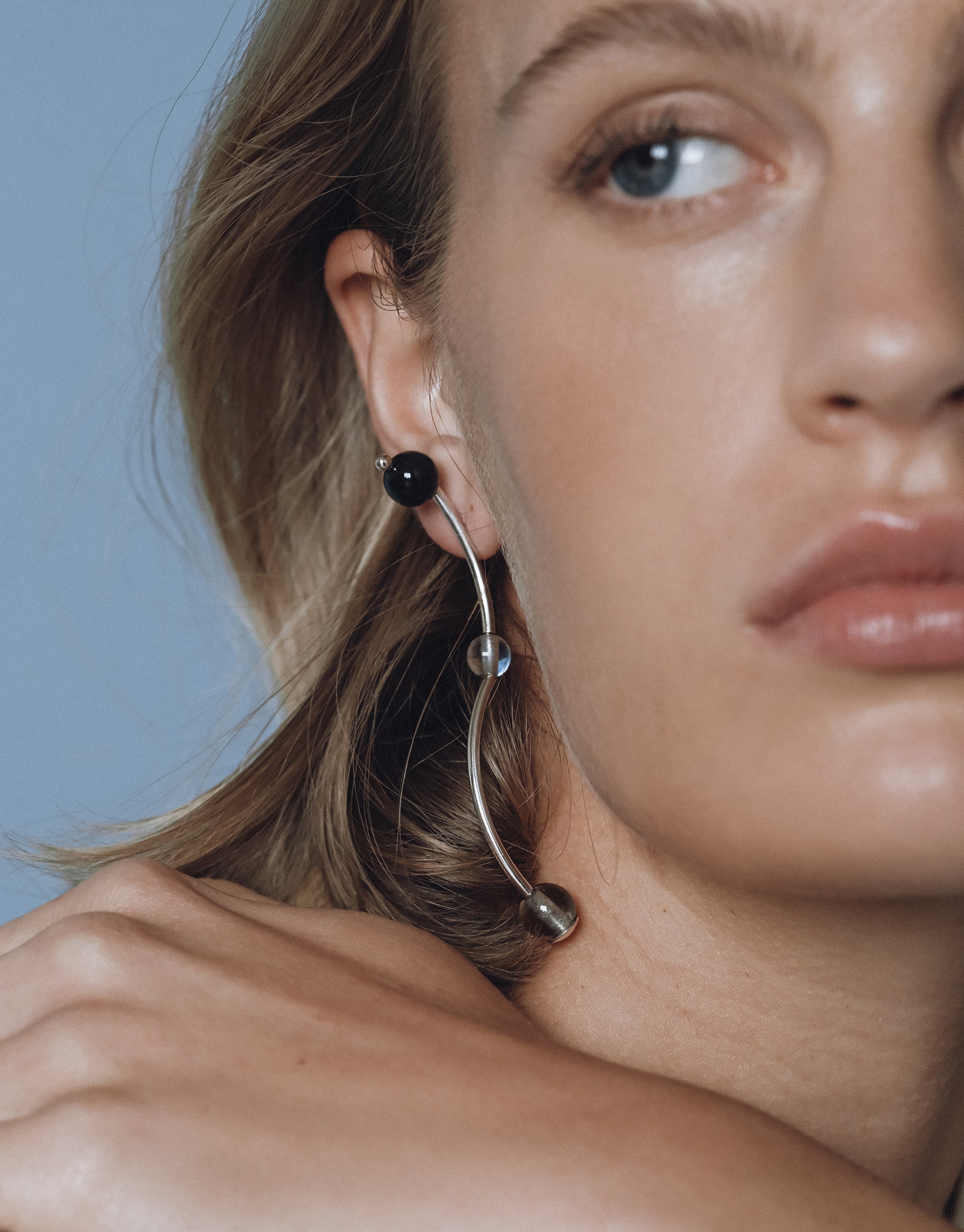 Curved silver Halo Earrings with black and clear glass spheres, shown on ear against blue background - CLED
