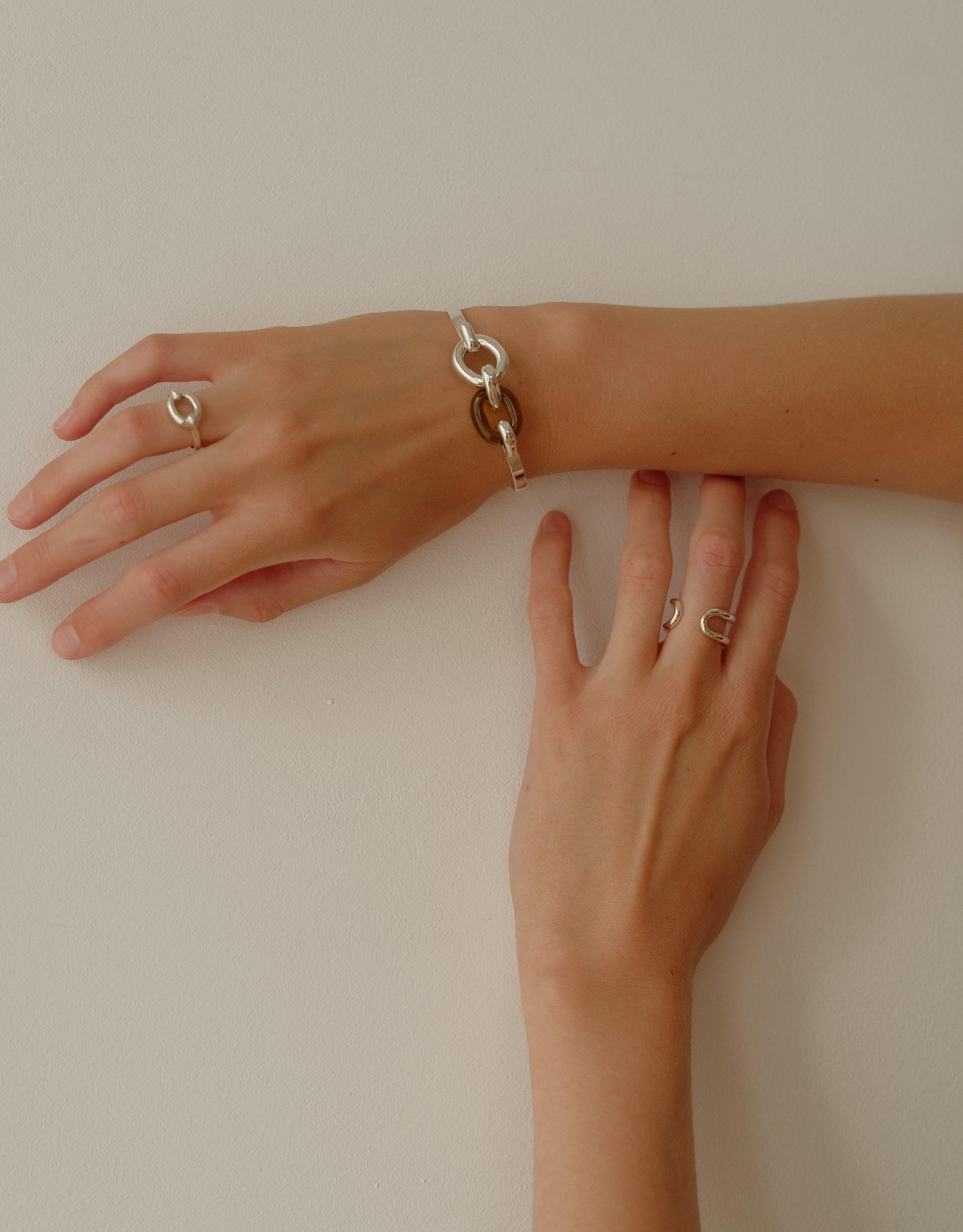 Elegant Loop Hook Bracelet from CLED's In The Loop collection, showcased on a model's wrist alongside matching rings. The silver-toned bracelet features interconnected loops, symbolizing unity and upcycling. Loop Hook Bracelet by CLED.