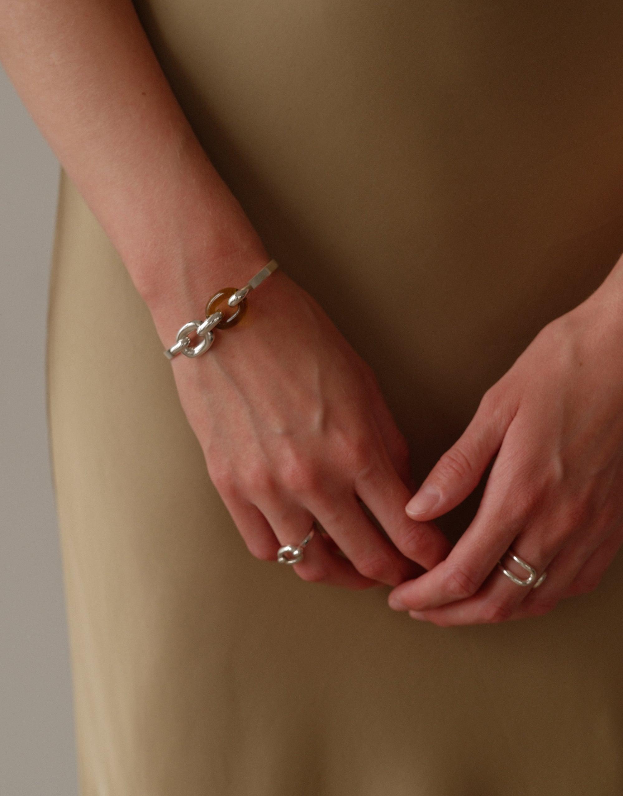 Elegant Loop Hook Bracelet from the upcycled In The Loop collection, showcasing a sleek silver design on a model's wrist. Paired with matching rings, symbolizing unity and connection. Sustainable jewelry by CLED, featuring the Loop Hook Bracelet.