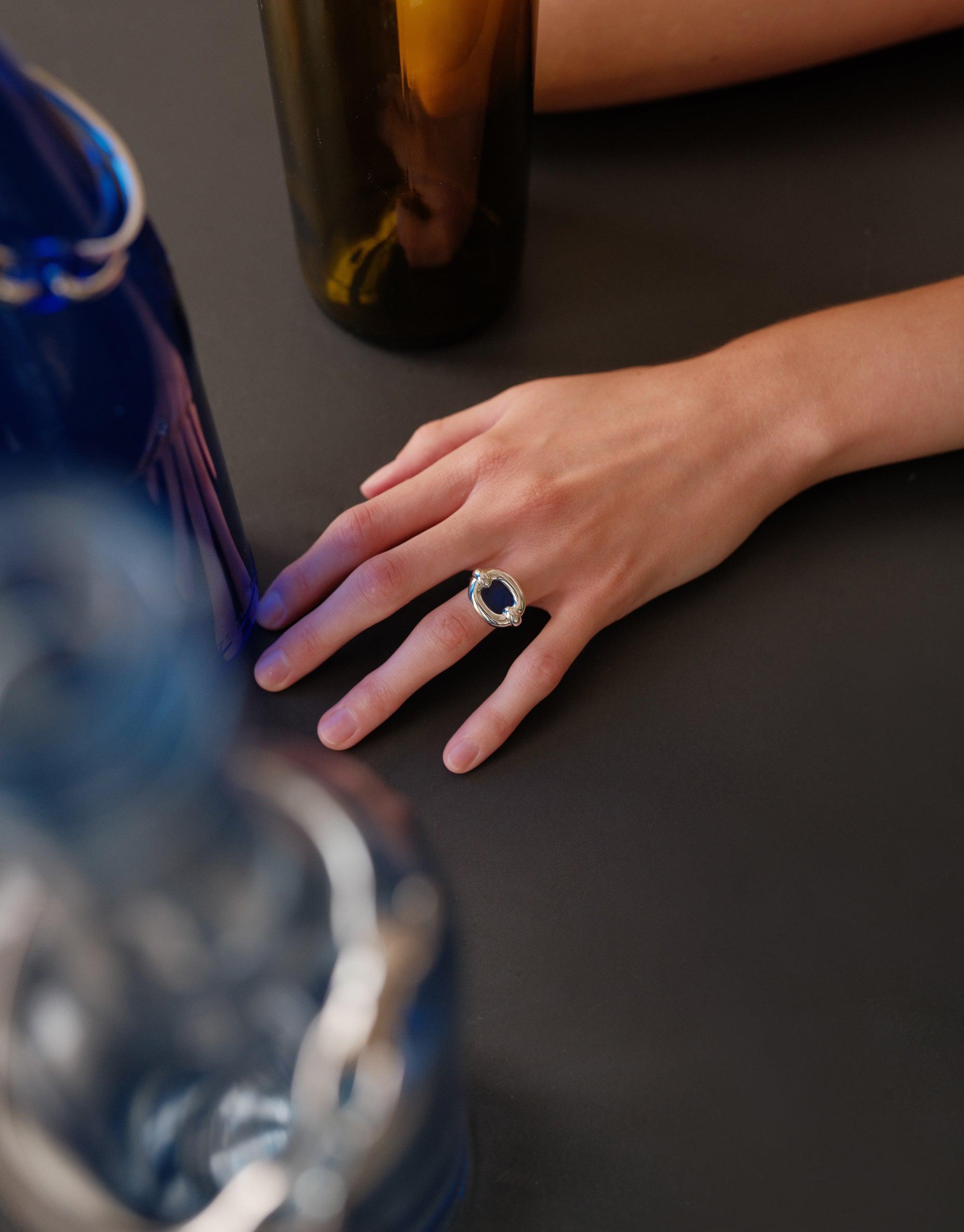 Elegant hand wearing Core Loop Ring | Large, showcasing eco gem encased in seamless metal setting. Mirror-like surface reflects surrounding colors, highlighting ring's unique design and functionality. Stylish accessory for everyday wear or special occasions by CLED.