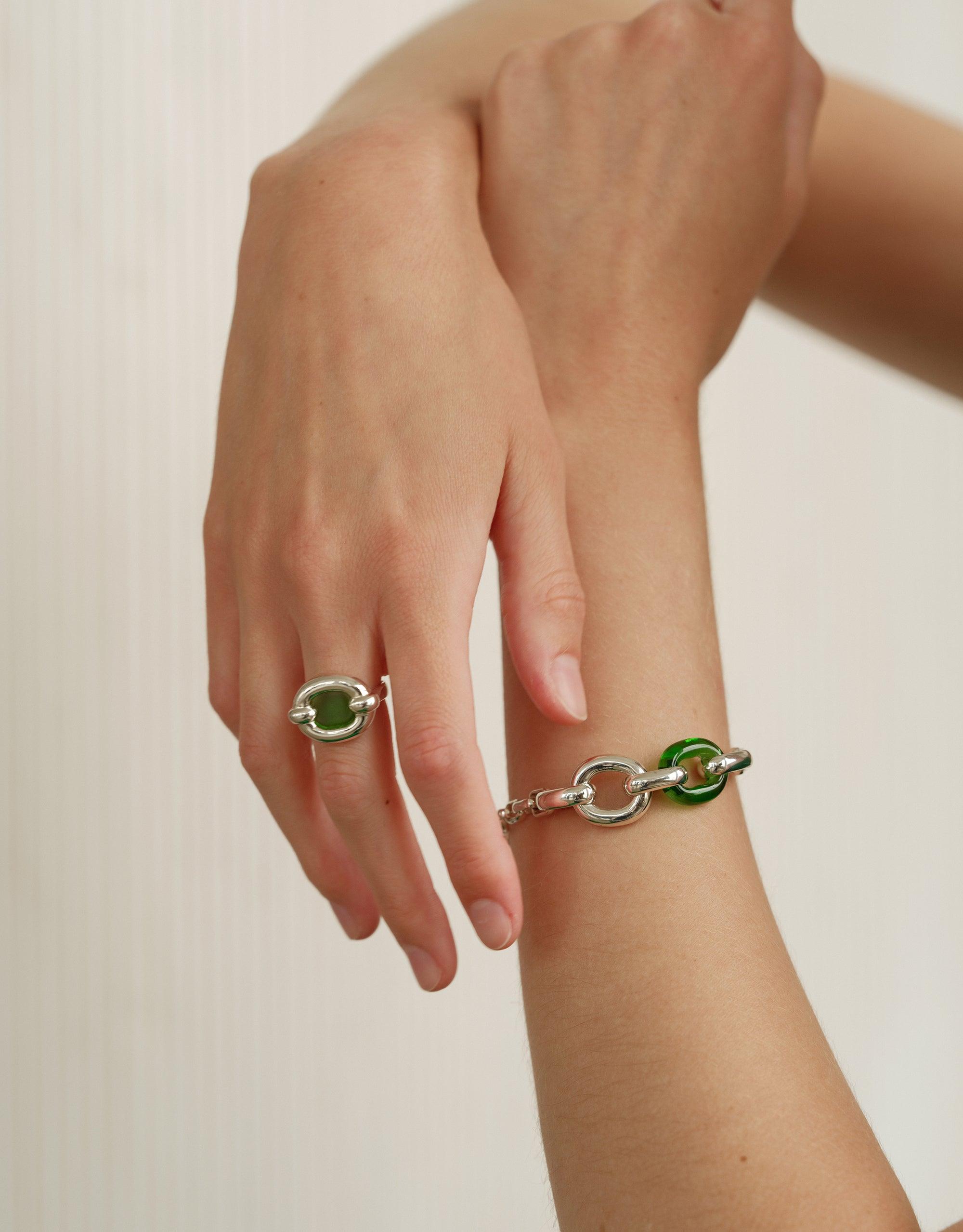 Elegant hands displaying Loop Chain Bracelet and matching ring, showcasing silver and green upcycled elements. Sustainable jewelry symbolizing unity and connection. Stylish accessories from the In The Loop collection by CLED.