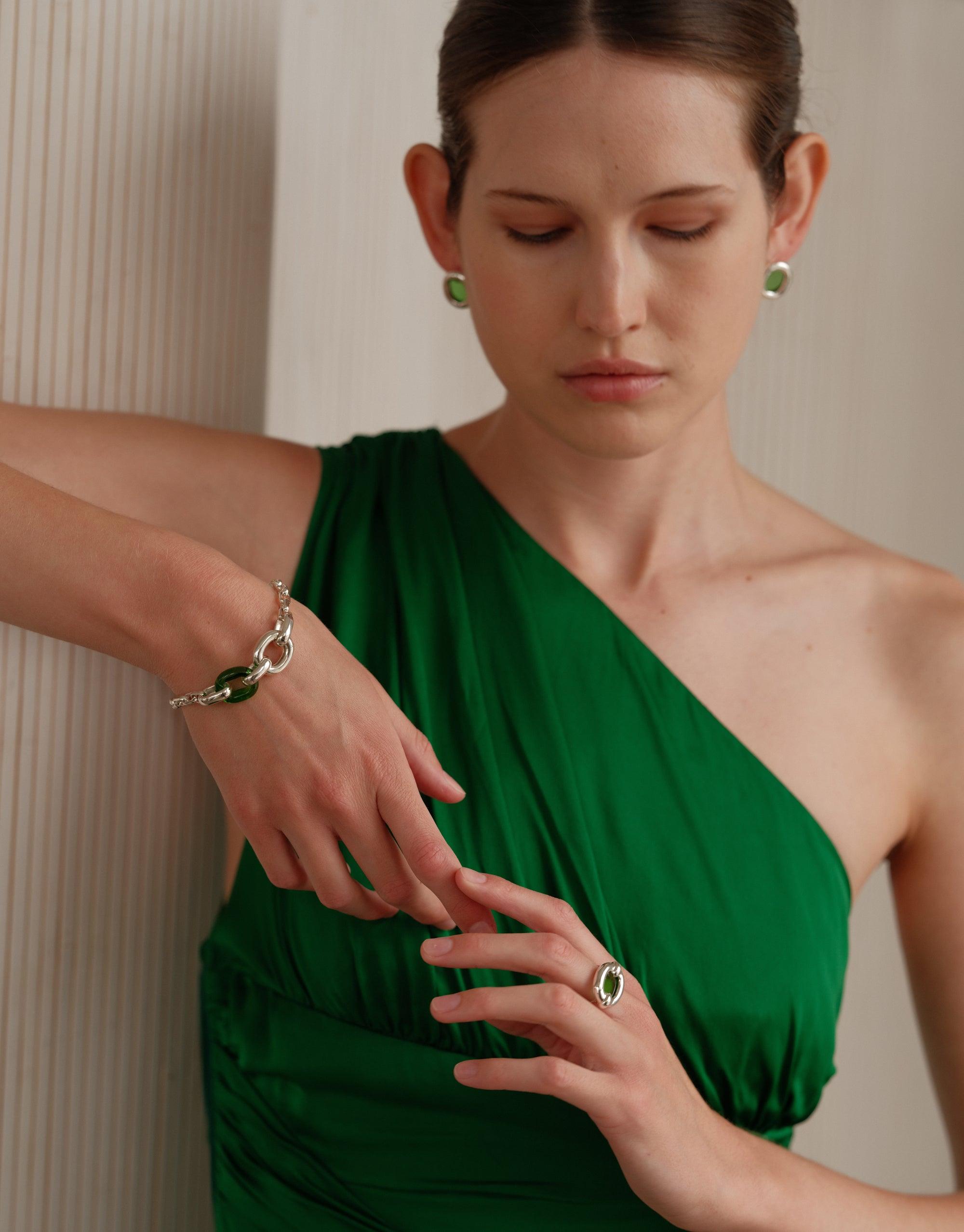 Elegant silver Loop Chain Bracelet worn by model in green one-shoulder dress, showcasing sustainable jewelry design. Part of the In The Loop collection, symbolizing unity and upcycling. Paired with matching ring and earrings. Loop Chain Bracelet by CLED.