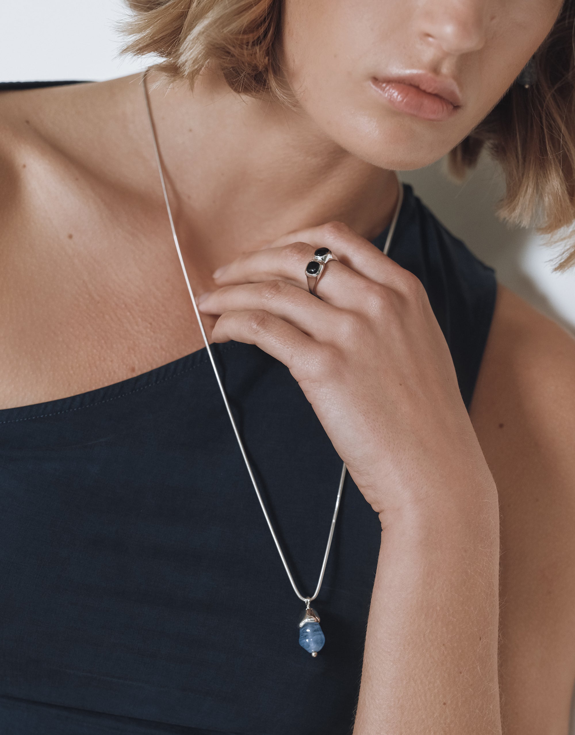 Model wearing Solace Drop Necklace with blue glass pendant on silver snake chain, paired with black top and ring - CLED