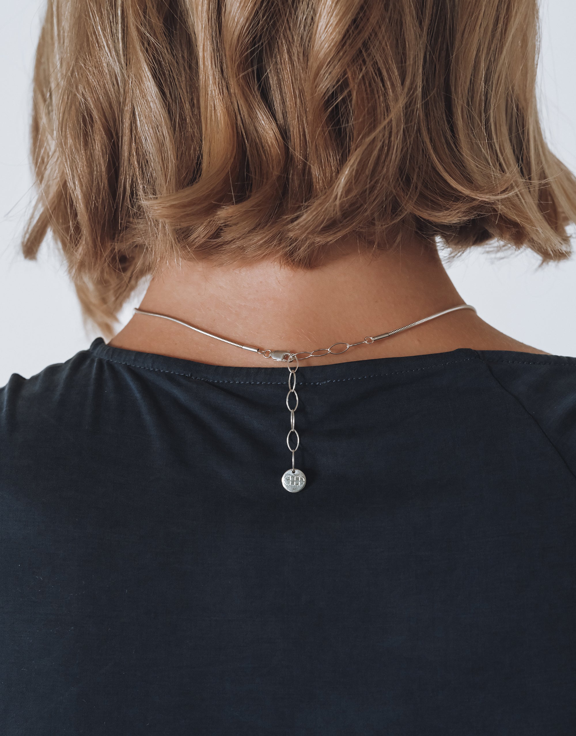 Silver Solace Drop Necklace with delicate glass pendant on snake chain, worn against black top - CLED