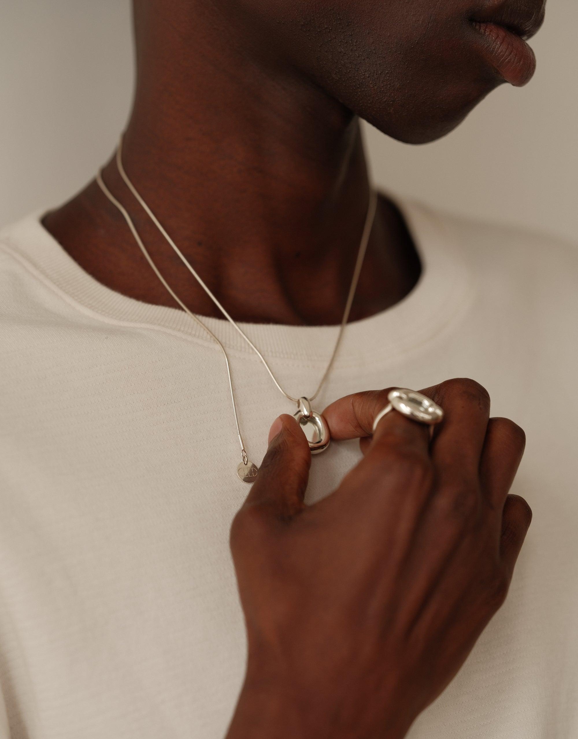 Elegant Core Loop Necklace with snake chain worn by model in white shirt, showcasing sustainable and unifying design. Delicate silver pendant held by hand, symbolizing connection and upcycling ethos. Core Loop Necklace | Snake Chain by CLED.