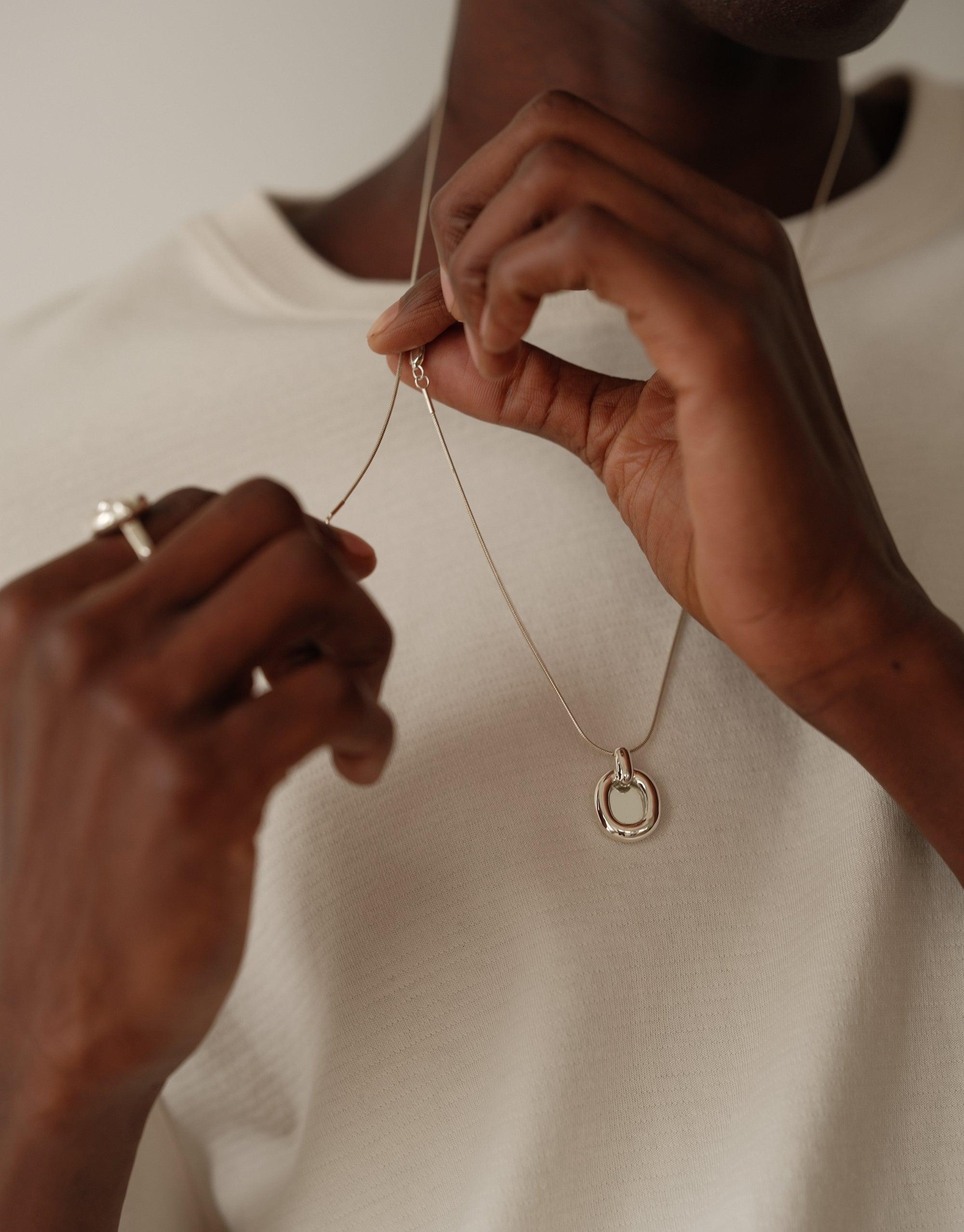 Hands delicately holding a sleek silver Core Loop Necklace with Snake Chain, showcasing its elegant design against a white background. The necklace symbolizes unity and upcycling, embodying CLED's commitment to sustainable fashion. Core Loop Necklace | Snake Chain by CLED.
