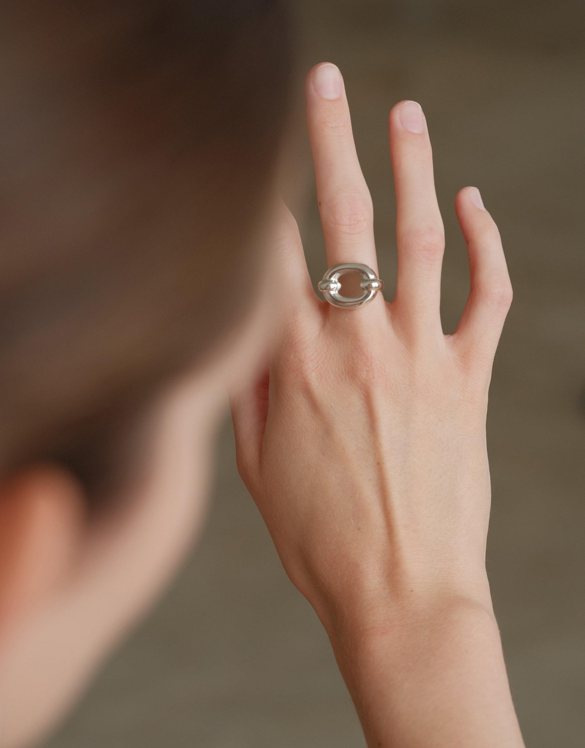 Hand displaying Core Loop Ring | Large, featuring a unique metal design with an eco gem encased in the center. The ring's mirror-like surface reflects light, showcasing its versatile functionality and elegant aesthetic. A stylish accessory by CLED.