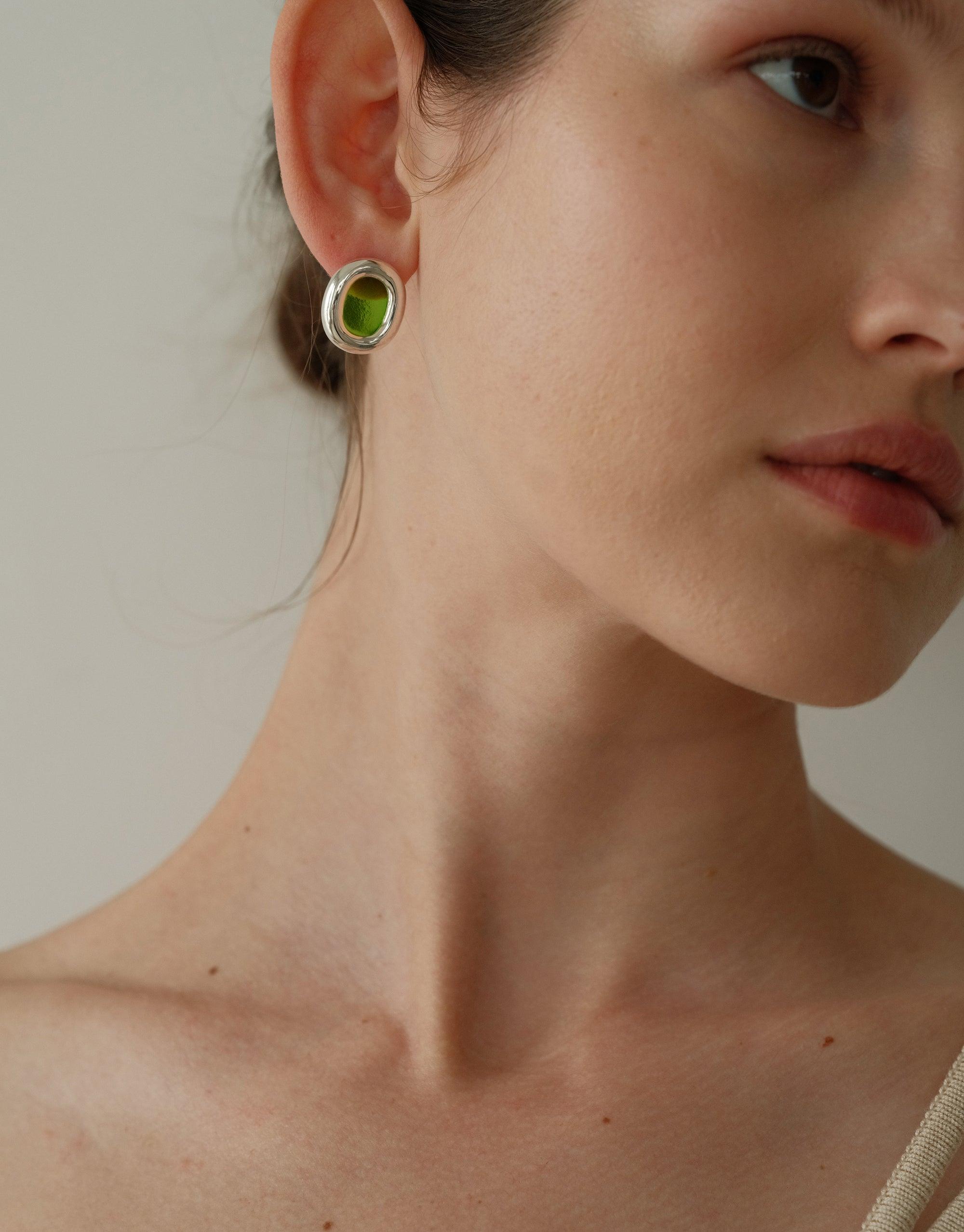 Large circular earring with green center, part of the Core Loop Earrings collection, showcased on a model's ear against a neutral background. Upcycled jewelry design symbolizing unity and connection. Sustainable fashion accessory by CLED. Core Loop Earrings | Large.