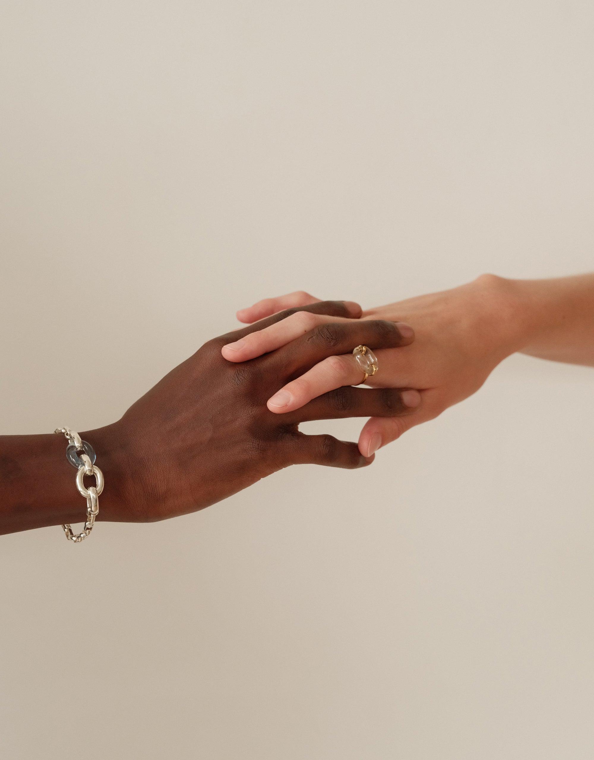 Two hands of different skin tones gently touching, showcasing the Loop Chain Bracelet on one wrist. A symbol of unity and connection, representing CLED's upcycling mission and the In The Loop collection. Loop Chain Bracelet by CLED.