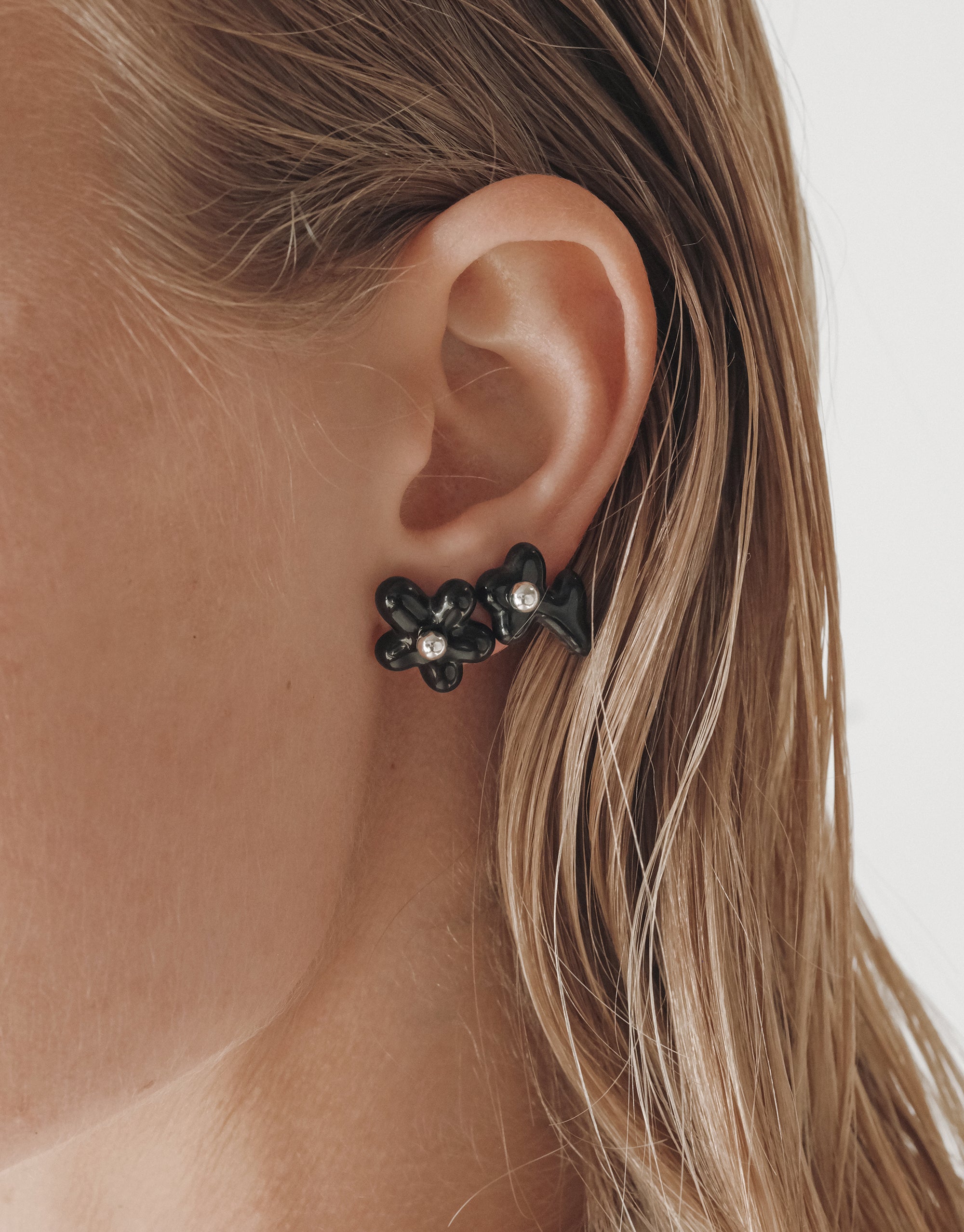 Stylish black Petal Icon Stud Earrings with floral design and crystal accents shown on ear, handcrafted by CLED