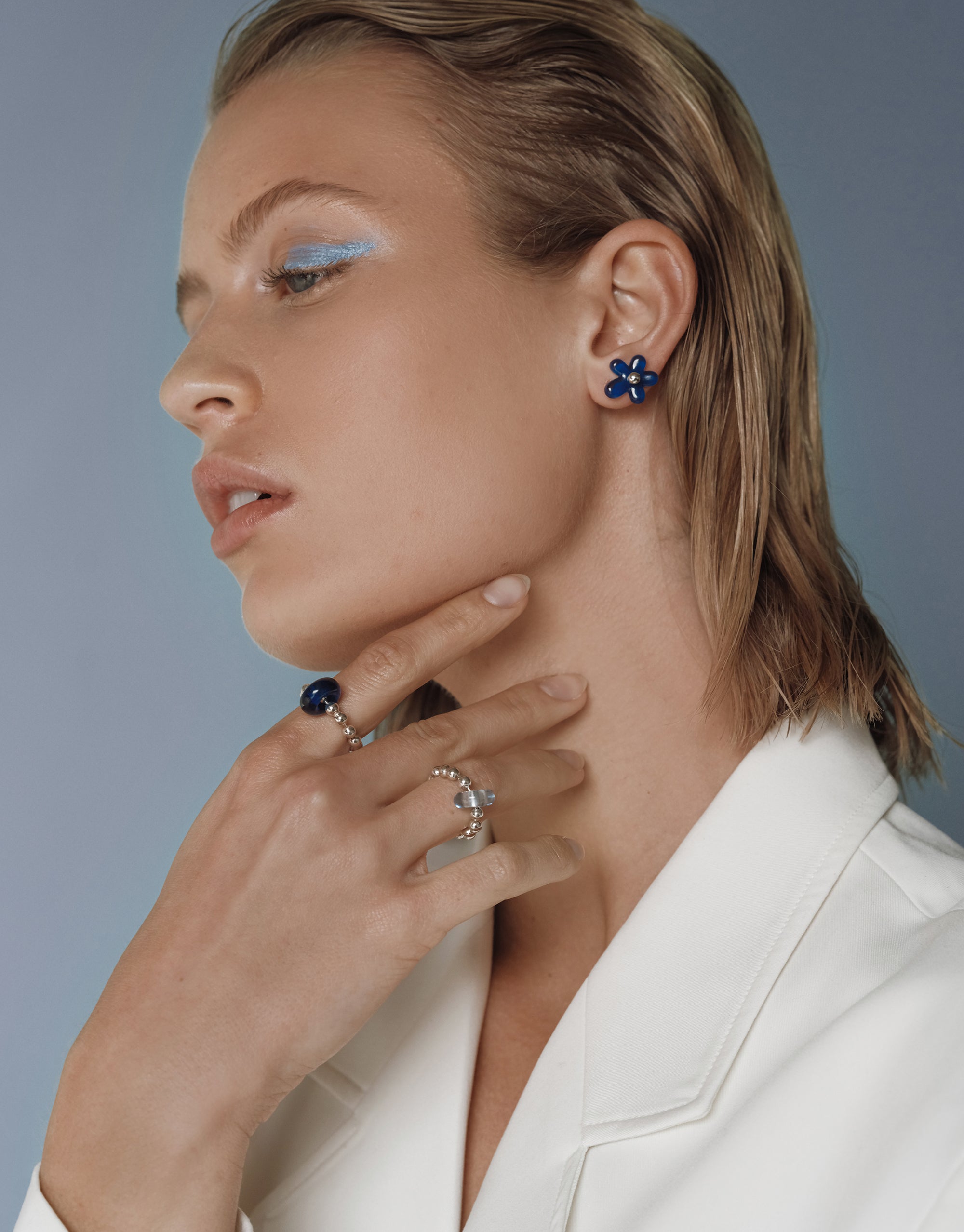 Elegant model wearing blue Petal Icon Stud Earrings in sterling silver, styled with rings and white blazer - CLED
