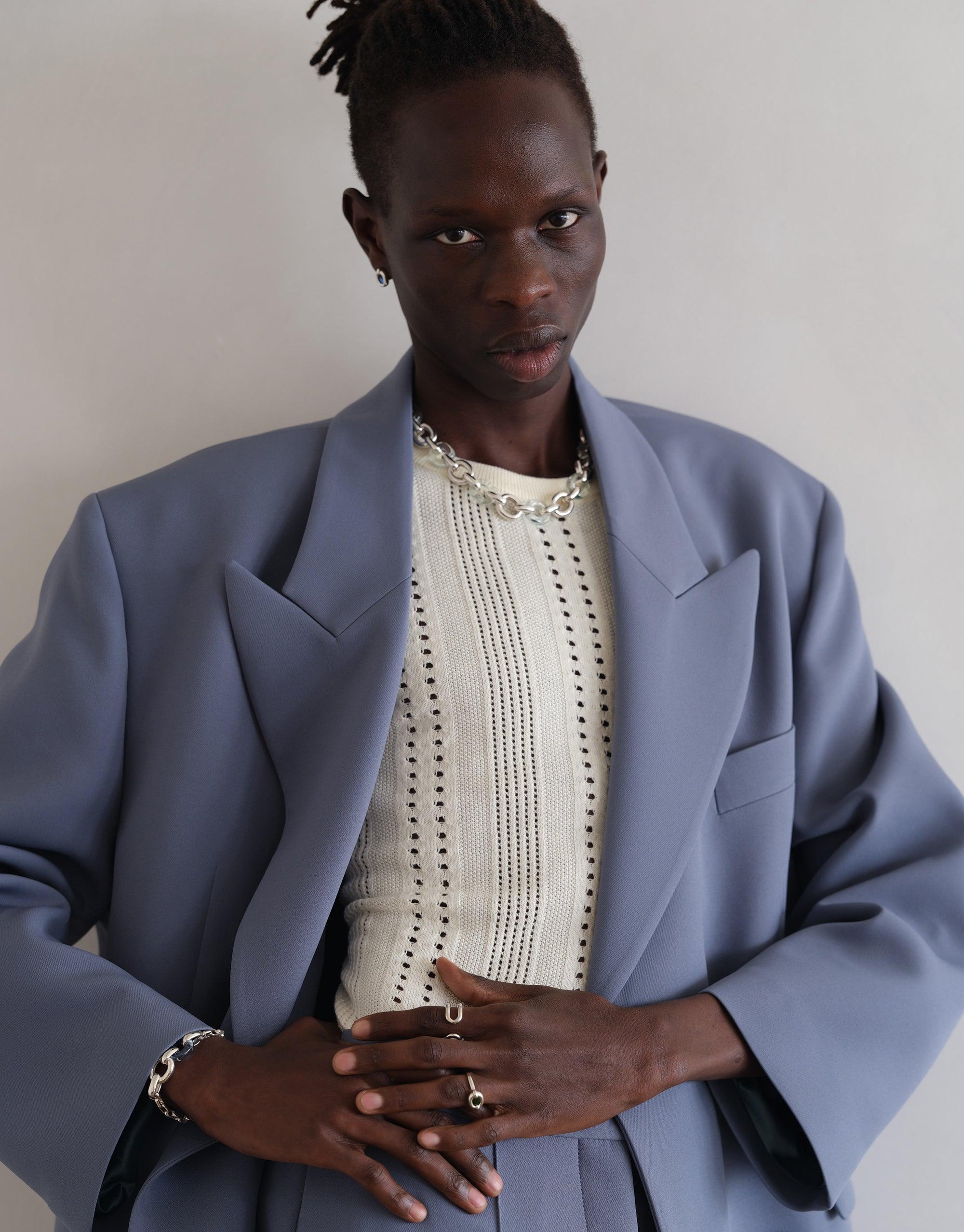 Stylish model wearing blue oversized blazer and white knit top, showcasing Loop Chain Bracelet. Elegant silver chain accessory complements modern, sustainable fashion aesthetic. CLED Loop Chain Bracelet.
