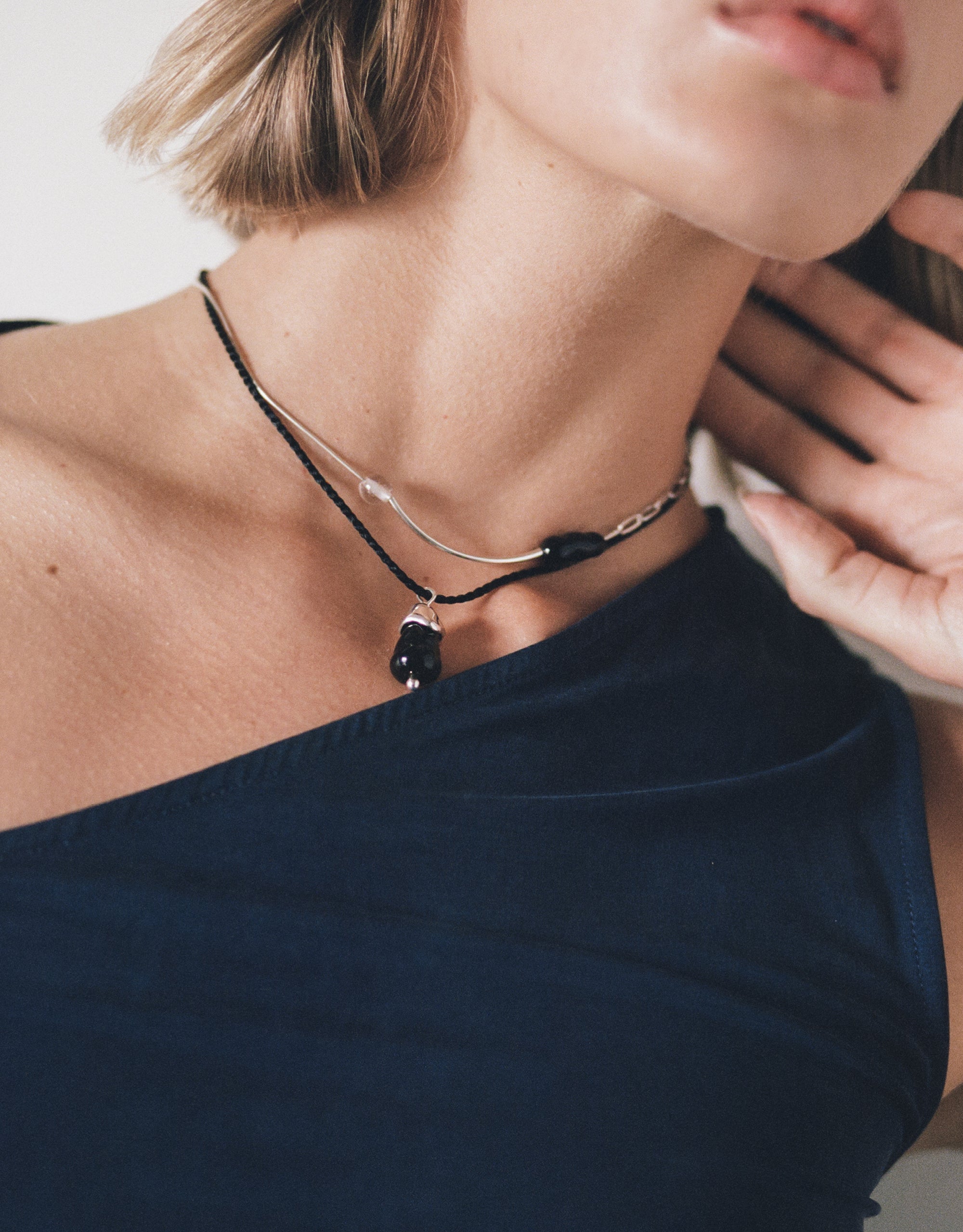 Still Necklace featuring asymmetrical silver curves and glass beads on black cord, styled with off-shoulder top - CLED