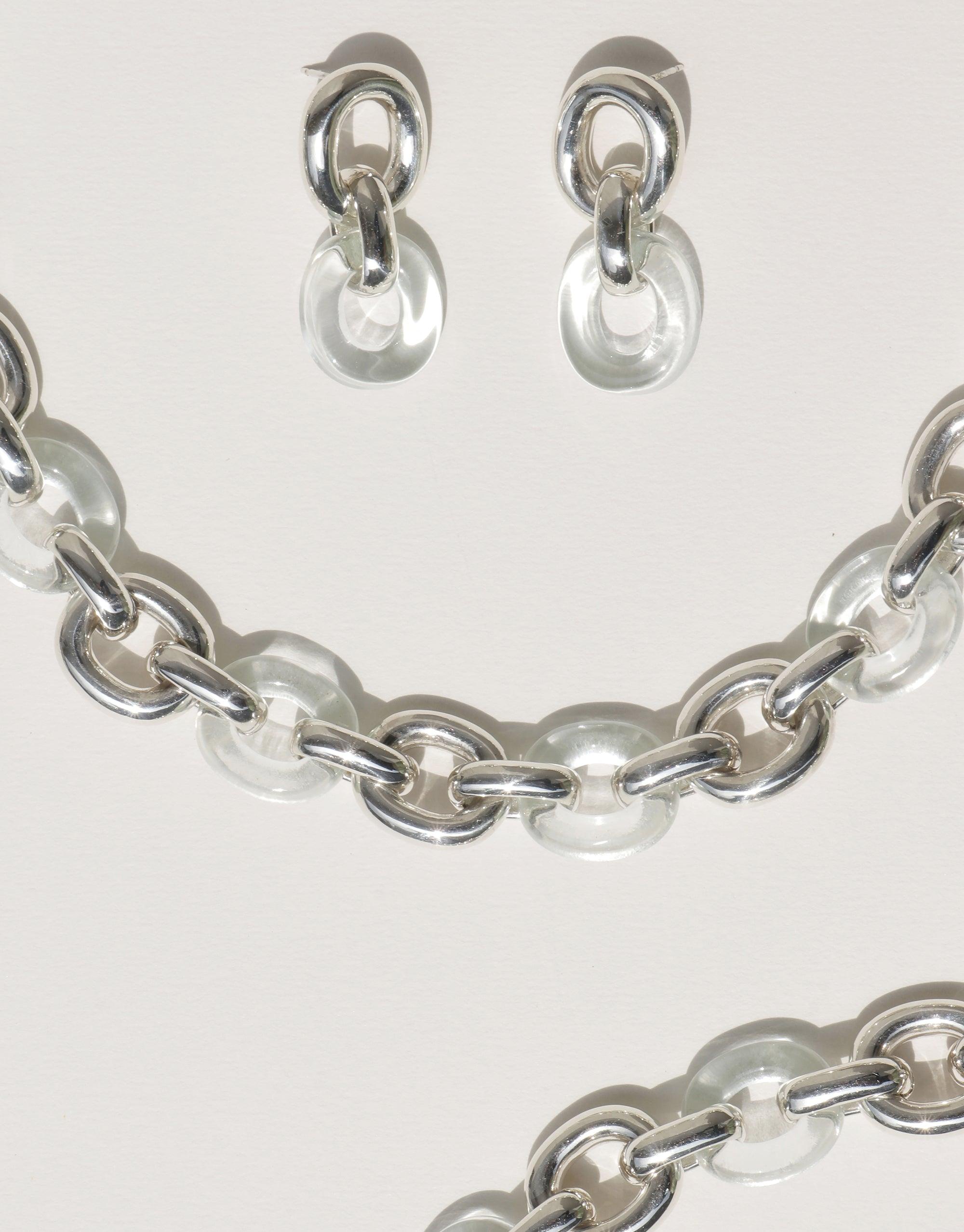 Elegant Connected Loop Earrings and matching necklace featuring alternating clear glass and silver metal links, symbolizing unity and upcycled design. Sustainable jewelry set showcasing CLED's commitment to transforming discarded materials into treasured accessories. Connected Loop Earrings by CLED.