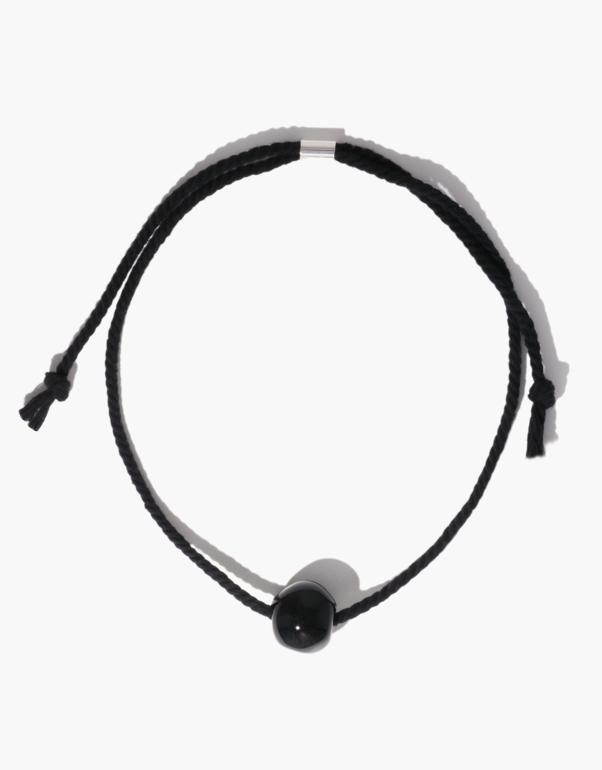 Black Pea Necklace featuring a single dark bead on an adjustable black cord. Inspired by nature's organic shapes and legume patterns, this minimalist design showcases growth and transformation. A versatile accessory that embodies simplicity and elegance. Black Pea Necklace by CLED.