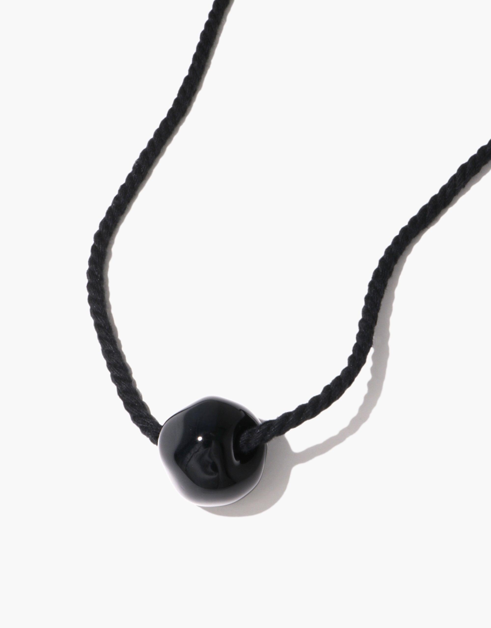 Black Pea Necklace featuring a single glossy black bead on a dark cord, inspired by nature's organic shapes and growth. Minimalist design capturing the essence of legume plants, symbolizing transformation and creativity. Elegant and versatile accessory. Black Pea Necklace by CLED.