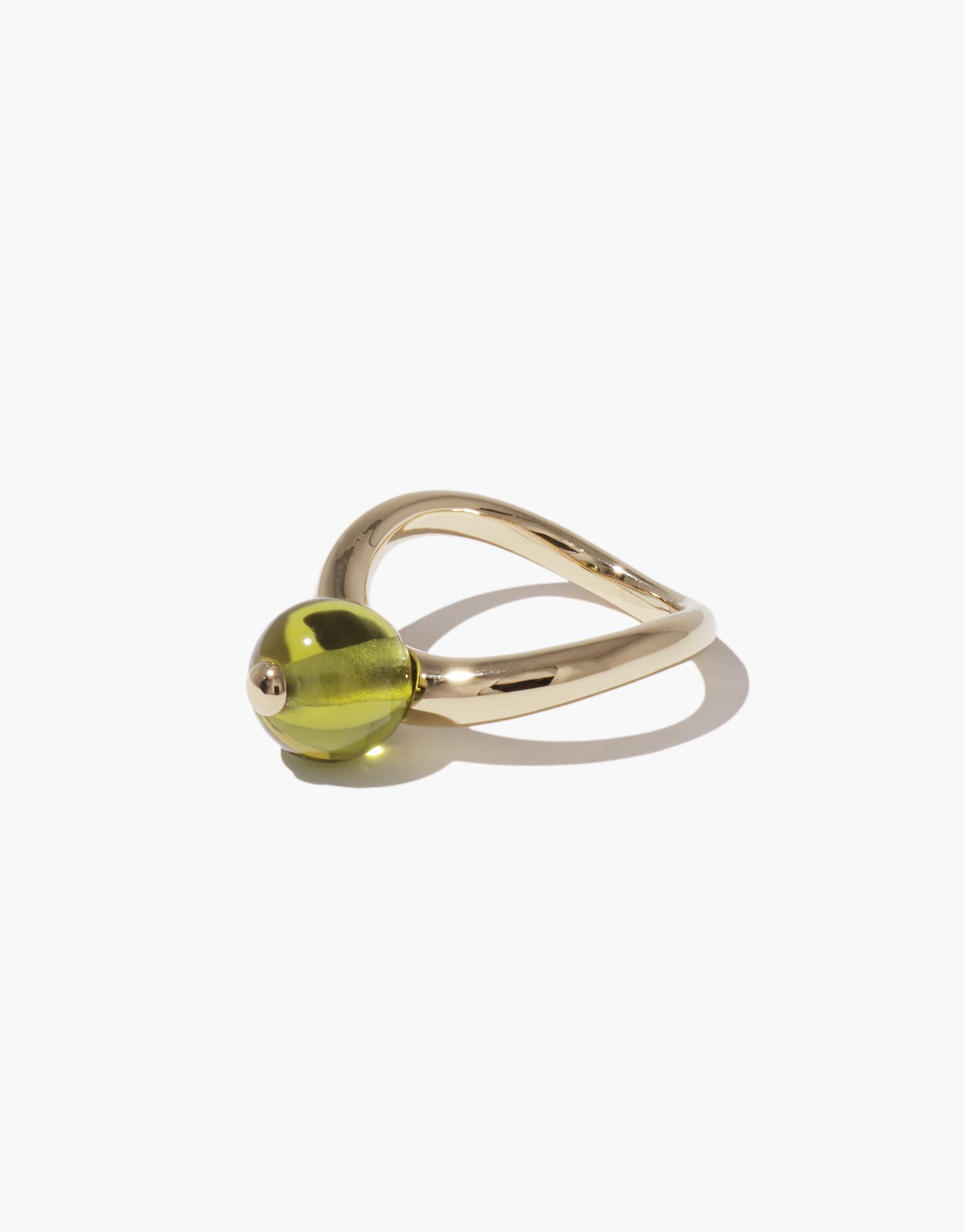 Elegant gold-toned ring with curved band and green spherical accent, inspired by nature's organic shapes. Pea Curve Ring | Large showcases a unique design reminiscent of a budding legume. Perfect for nature lovers and those appreciating sustainable, creative jewelry. CLED
