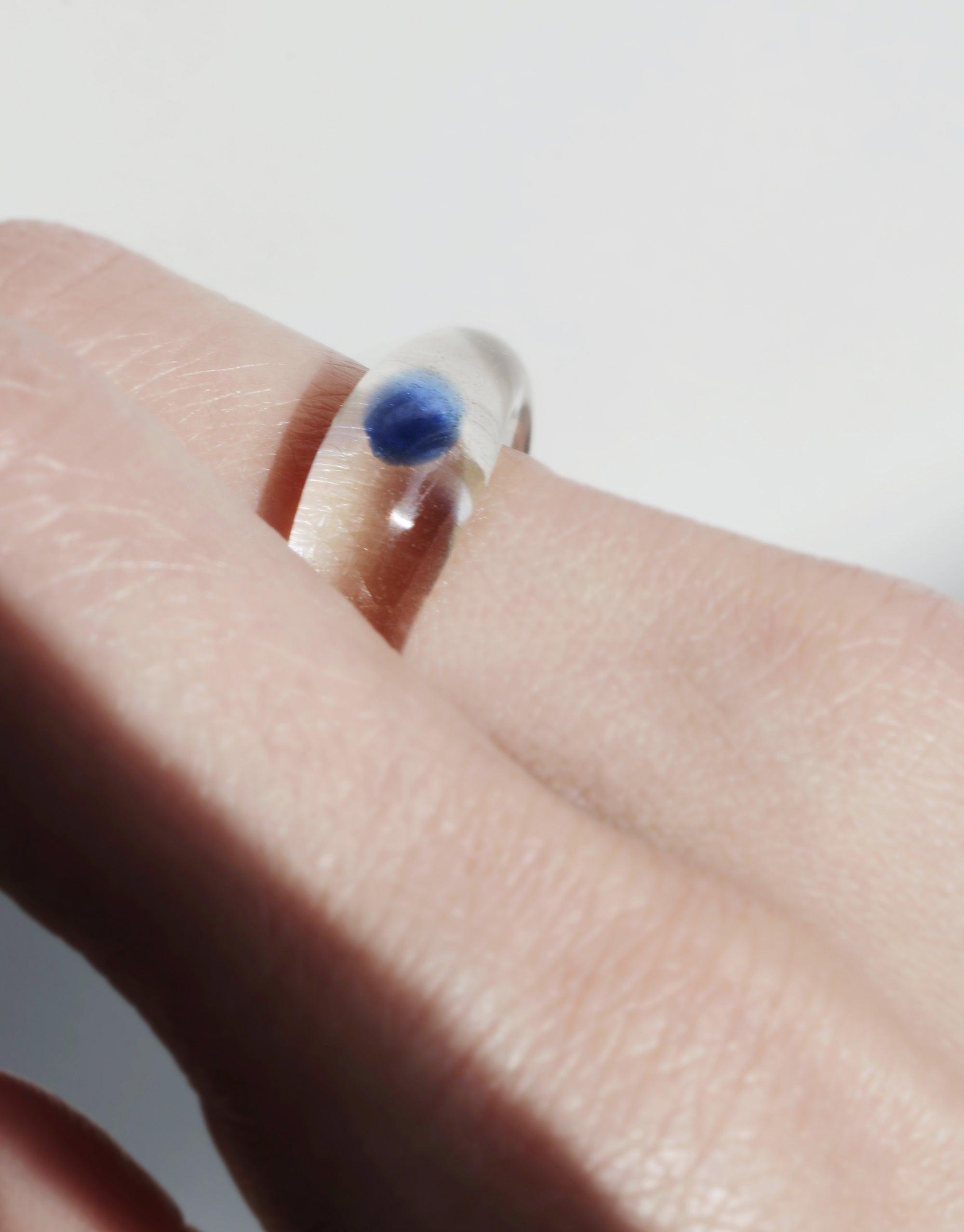 Close-up of the Blue Moon Ring on a finger, showcasing a silver band with a vibrant blue spherical stone. The ring's minimalist design highlights the captivating blue centerpiece, embodying enchanting elegance. Blue Moon Ring by CLED.