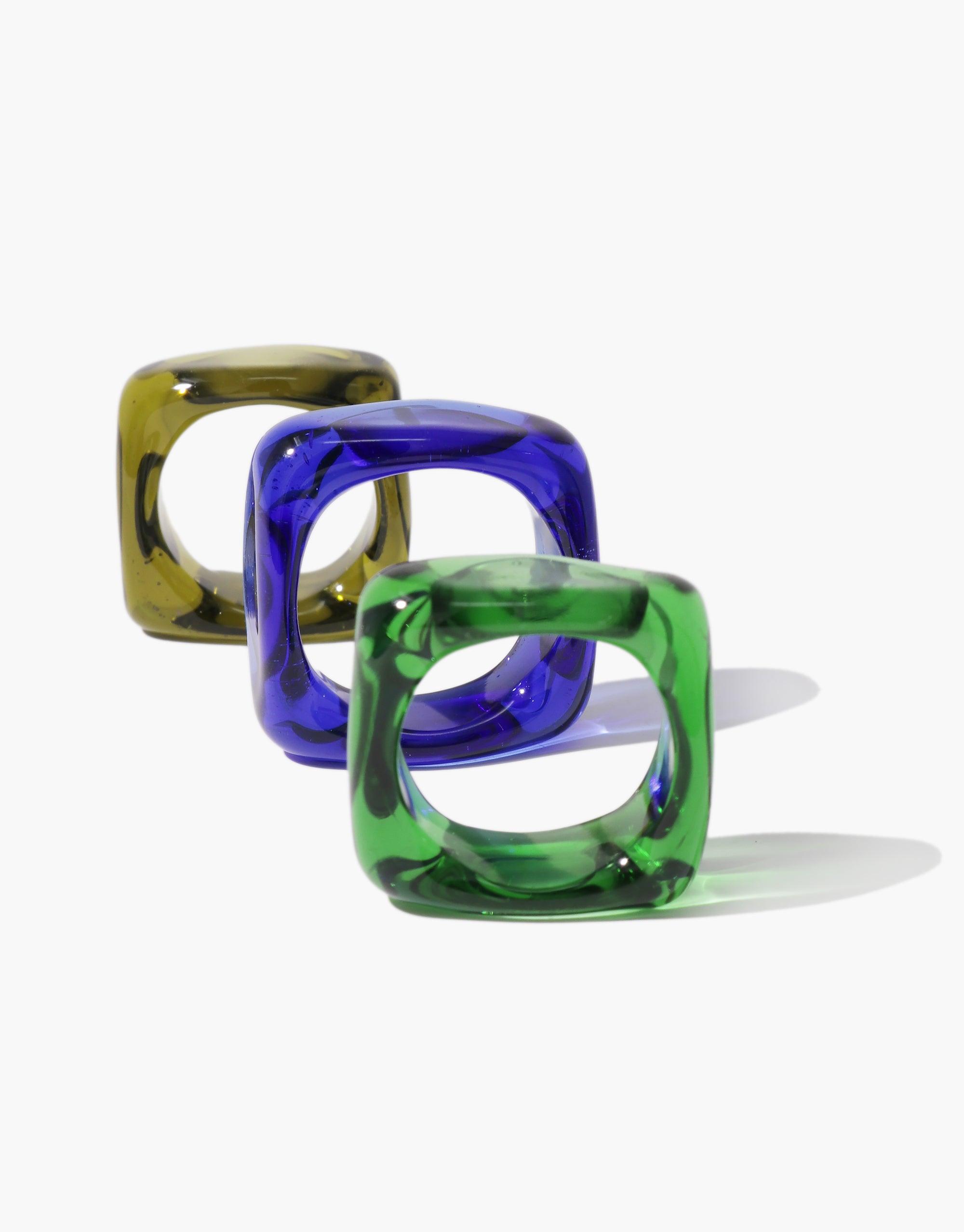 Three square-shaped glass rings in olive, blue, and green colors, showcasing unique translucent designs for the Engravable Dice Ring. These stylish and customizable accessories offer a modern twist on traditional jewelry, perfect for personalized engraving. CLED