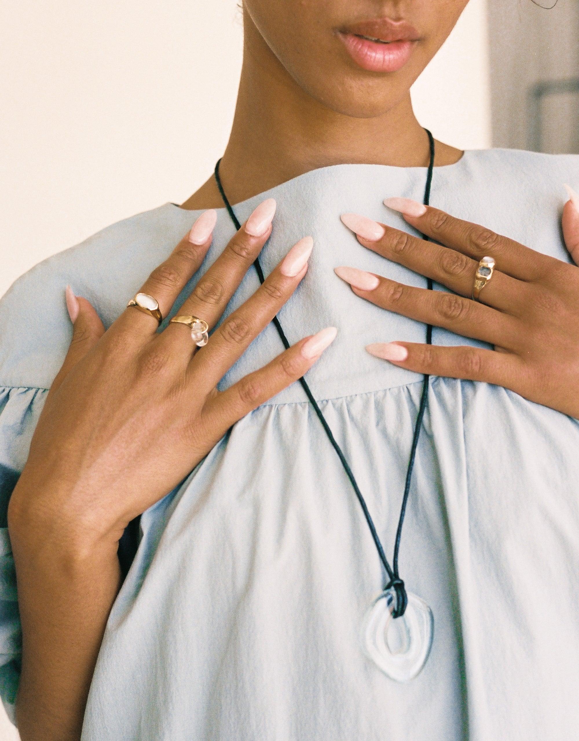 Close-up of hands wearing multiple rings, including the Oval Sculpture Ring, against a light blue blouse. Elegant jewelry display showcasing handcrafted design and eco-friendly materials. Oval Sculpture Ring by CLED.