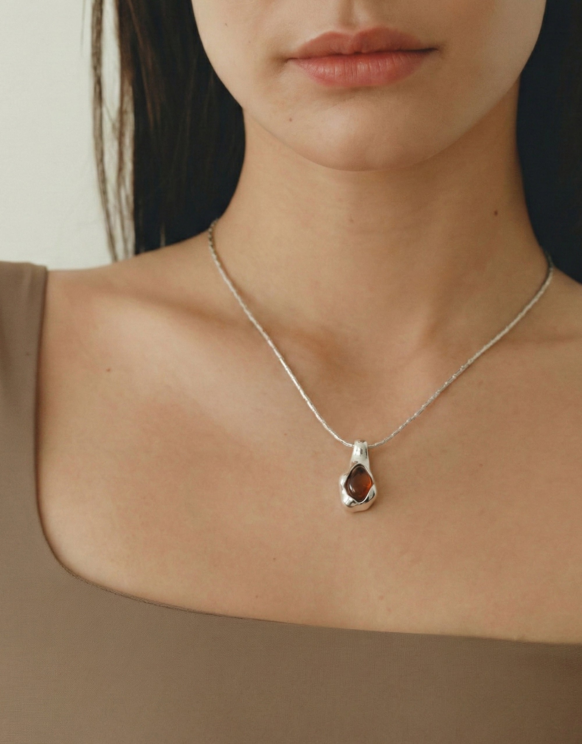 Silver necklace with a pendant with brown stone worn by a person
