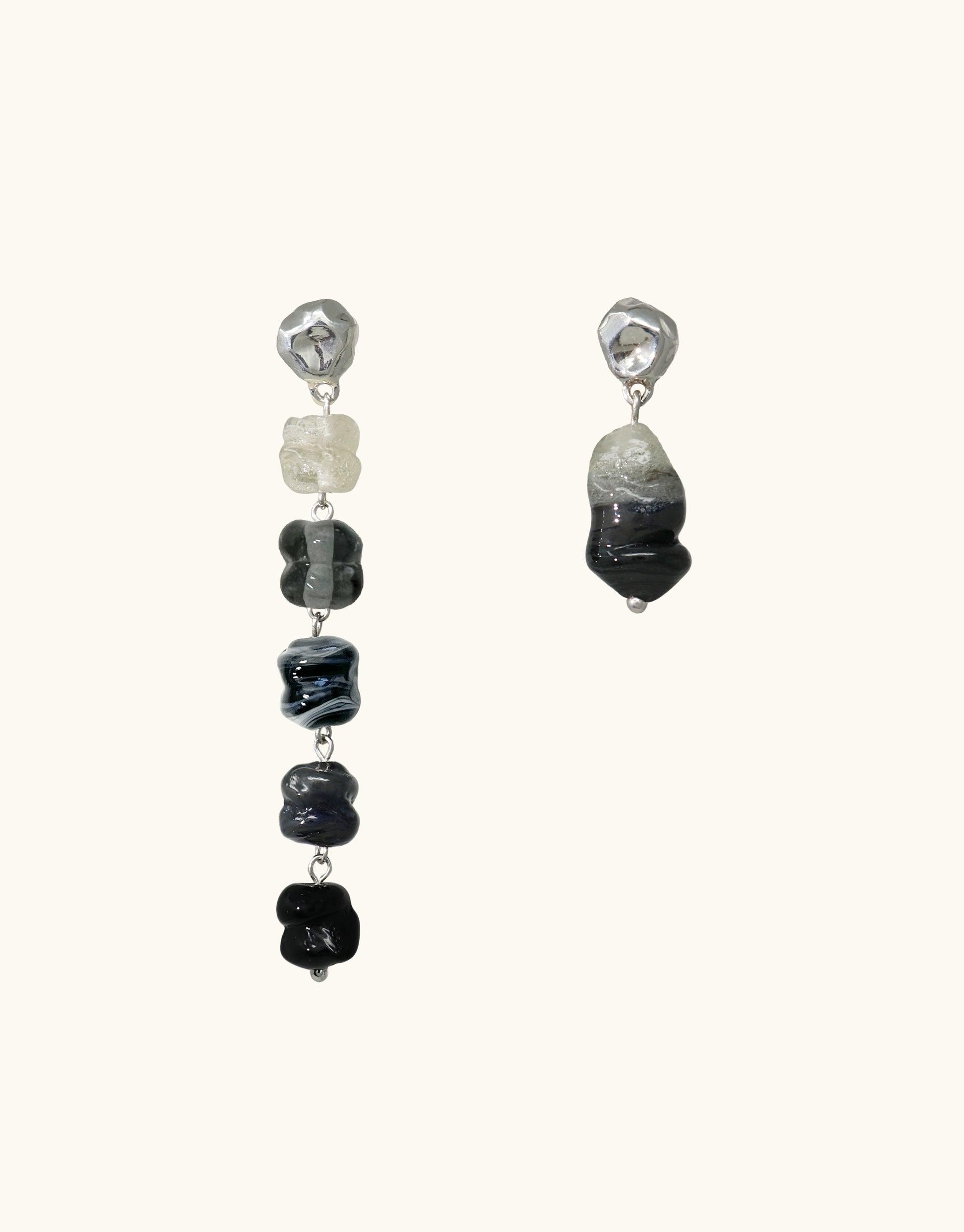 Asymmetric earrings featuring eco-friendly glass beads in shades of gray and black, inspired by basalt volcanic canyons. One earring longer with multiple beads, the other shorter. Handcrafted sustainable jewelry showcasing nature's beauty. Shades of Nature | Basalt Earrings by CLED