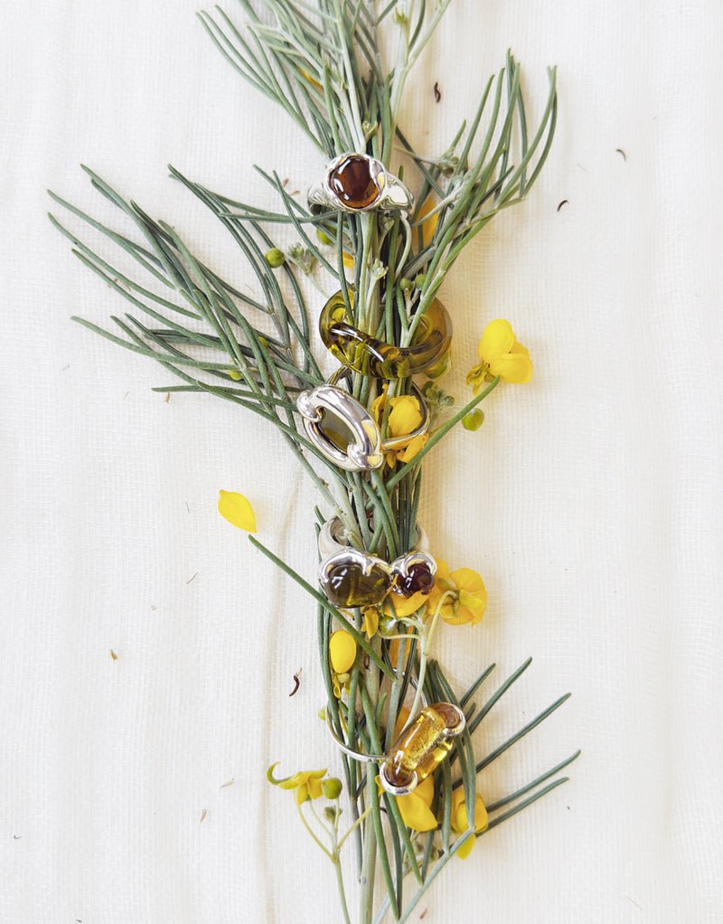 Decorative arrangement with greenery, yellow flowers, and metallic silver rings on a white background