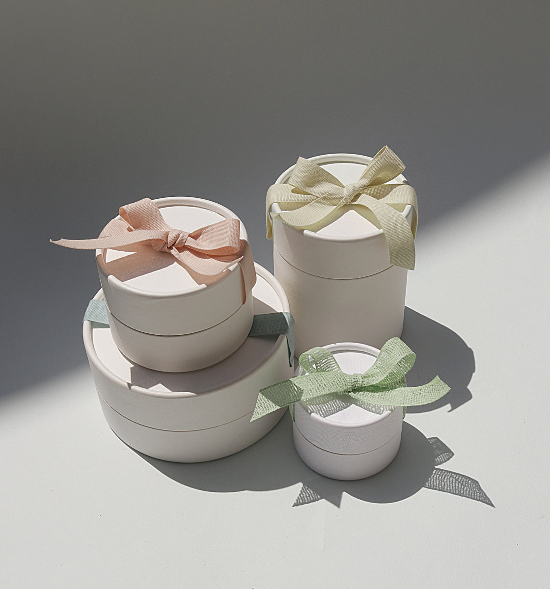A grouping of CLED's signature round cream-colored jewelry gift boxes in various sizes, tied with pastel pink, yellow, sage, and mint ribbon bows, styled in soft natural light.