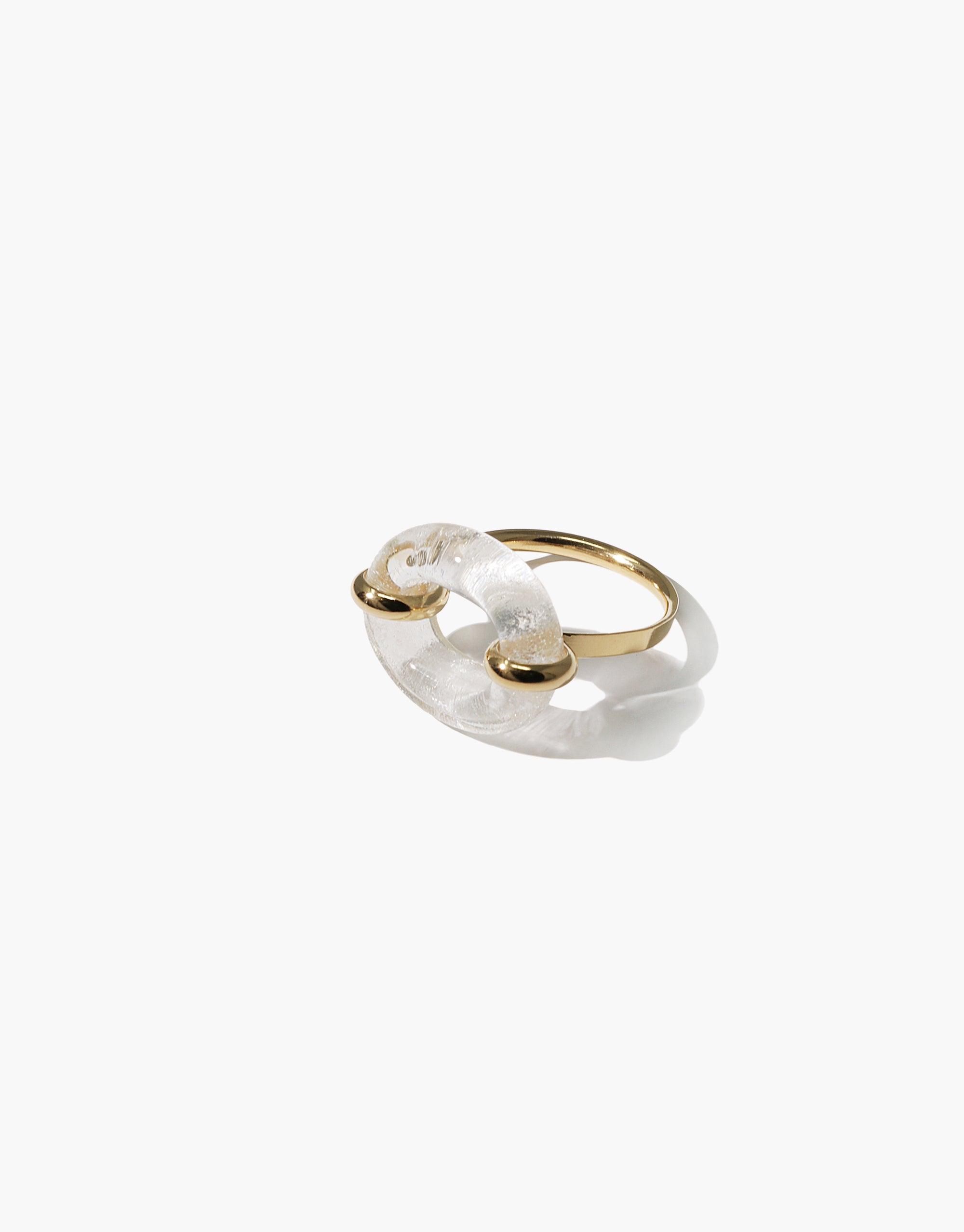 Unique gold-toned ring featuring a clear, loop-shaped element connected to a thin band. The In The Loop Ring symbolizes connection and solidarity with its interlocking design. Sustainable and stylish accessory by CLED.