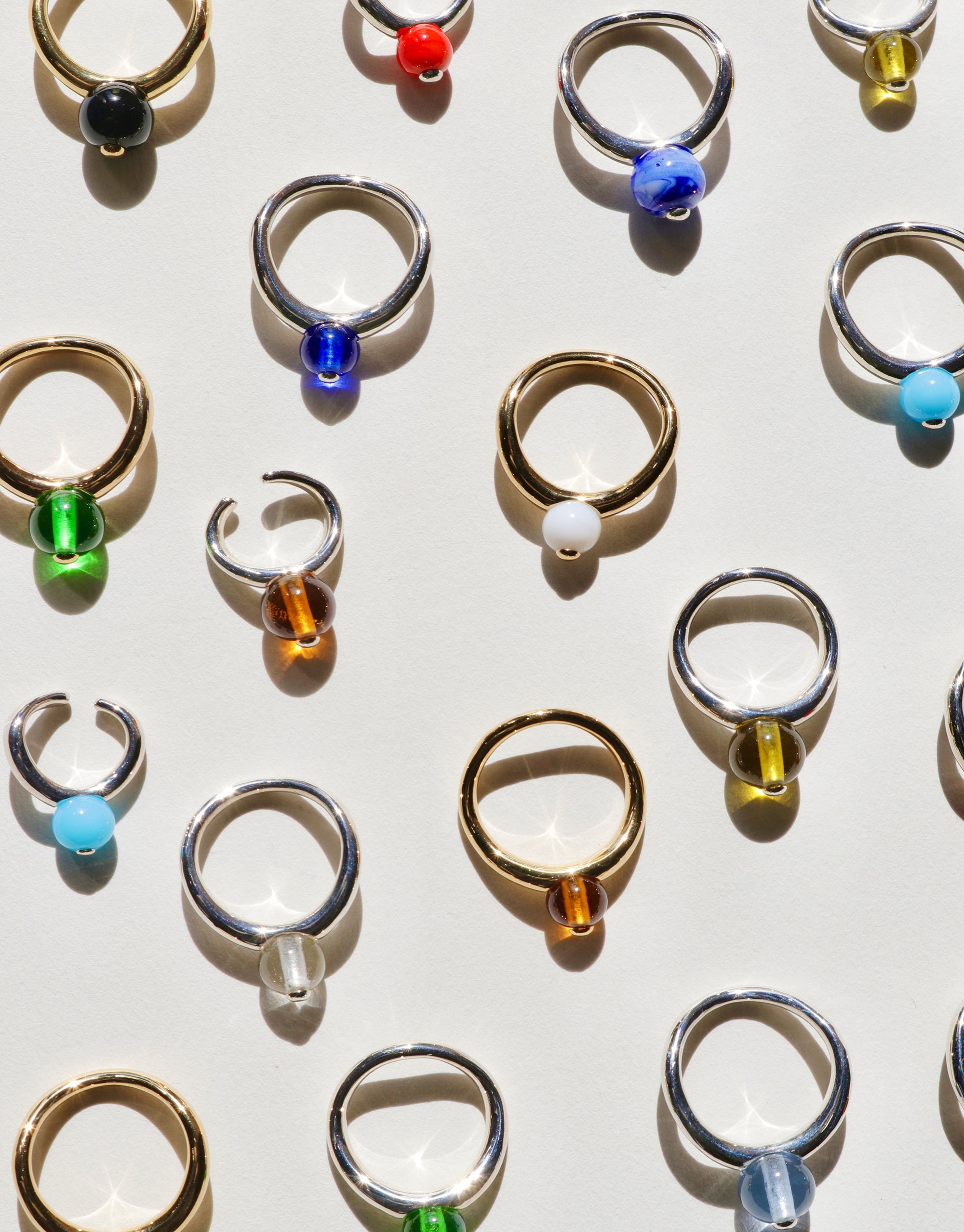Various color of rings and earrings arranged neatly on a white background, highlighting their unique styles inspired by pea shape.