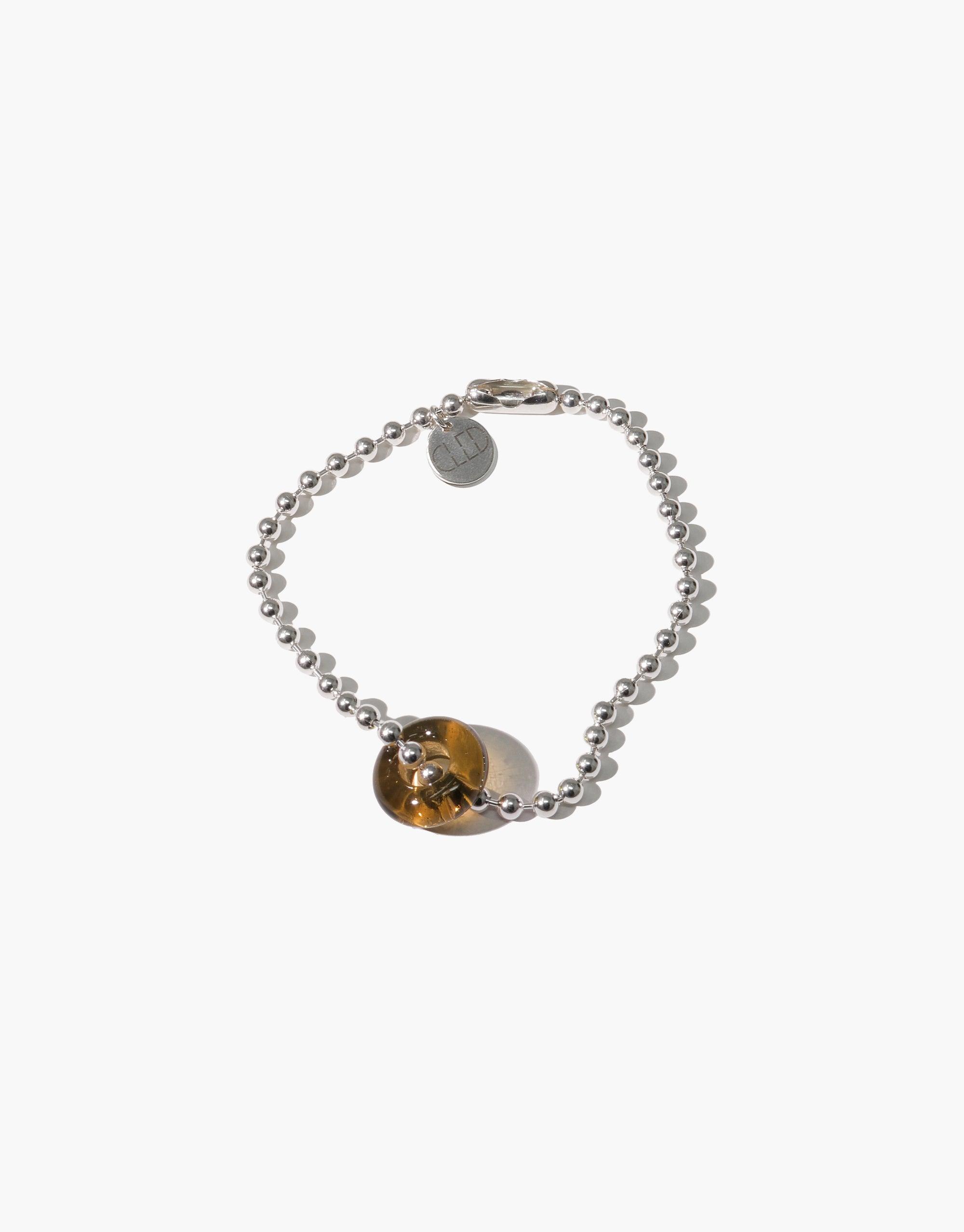 Donut Ball Bracelet featuring a silver beaded chain with a unique amber-colored glass bead, showcasing sustainable luxury and eco-friendly design. Handcrafted jewelry piece from the Rays of Light collection by CLED.