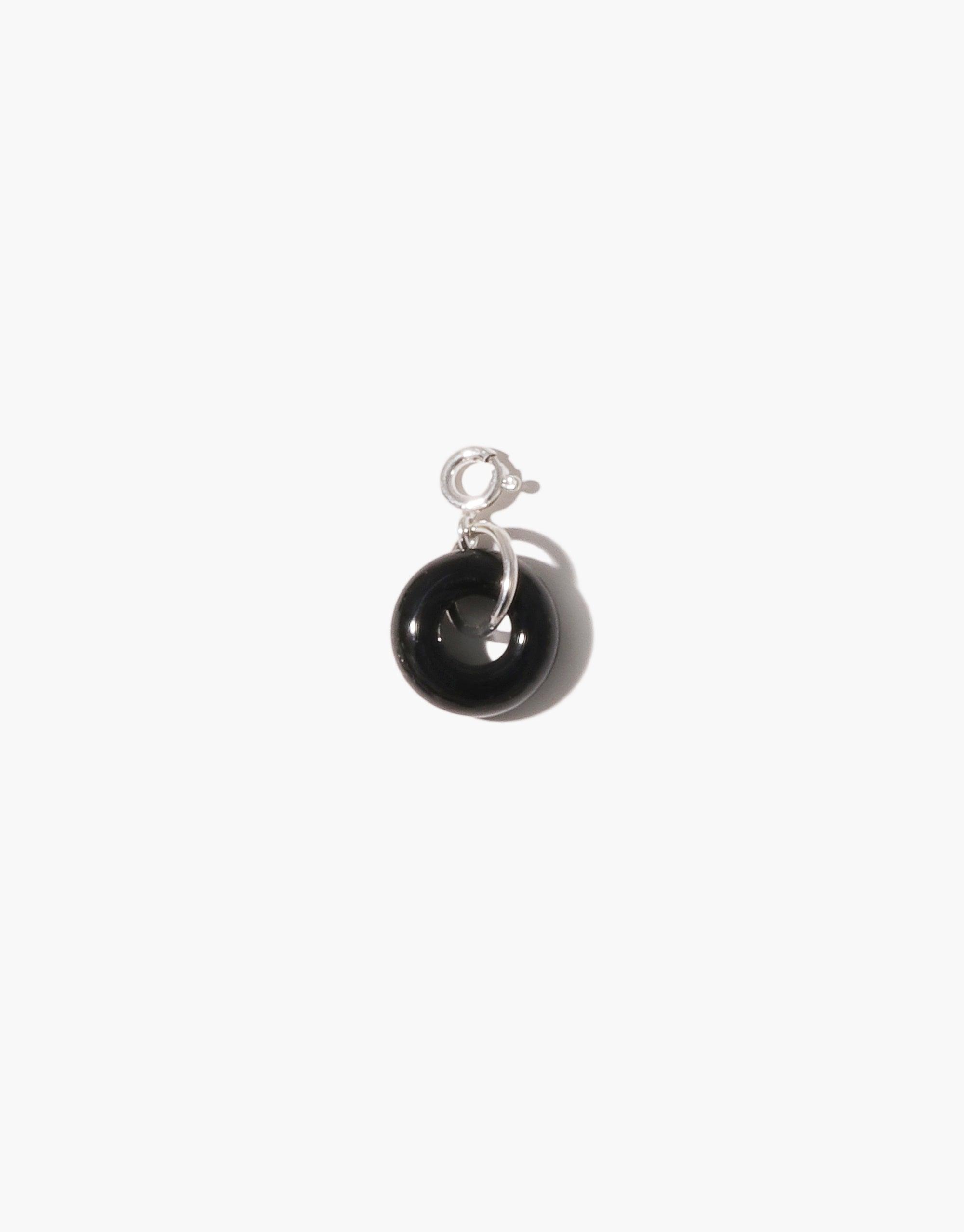 Sterling silver charm featuring a glossy black spherical pendant resembling a donut shape, perfect for adding to necklaces or bracelets. Handcrafted icon charm from upcycled glass, part of the Donut Icon Charm collection by CLED.