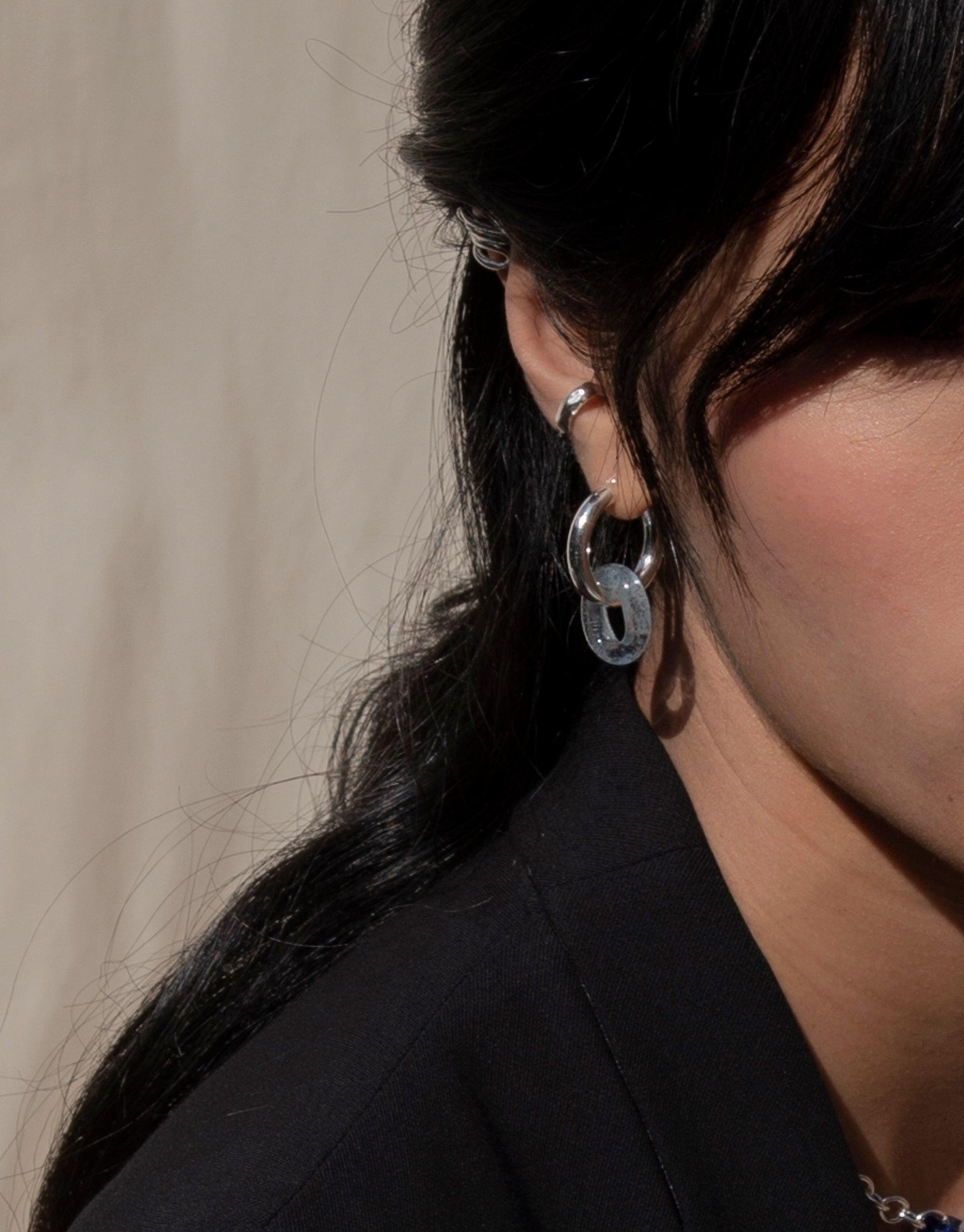 Close-up of a person wearing large silver hoop earrings with a unique looped design, showcasing the elegant and eco-friendly "In The Loop Hoops | Large" by CLED