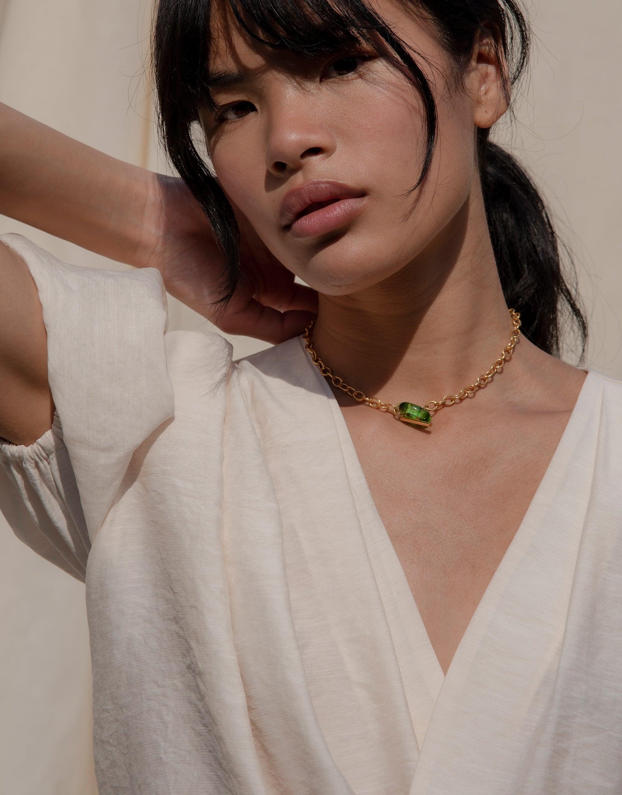 Elegant gold choker necklace with green eco gem accent worn by model in white v-neck top, showcasing the ITL Toggle Choker Necklace's delicate design and versatile style. Handcrafted sustainable jewelry by CLED.