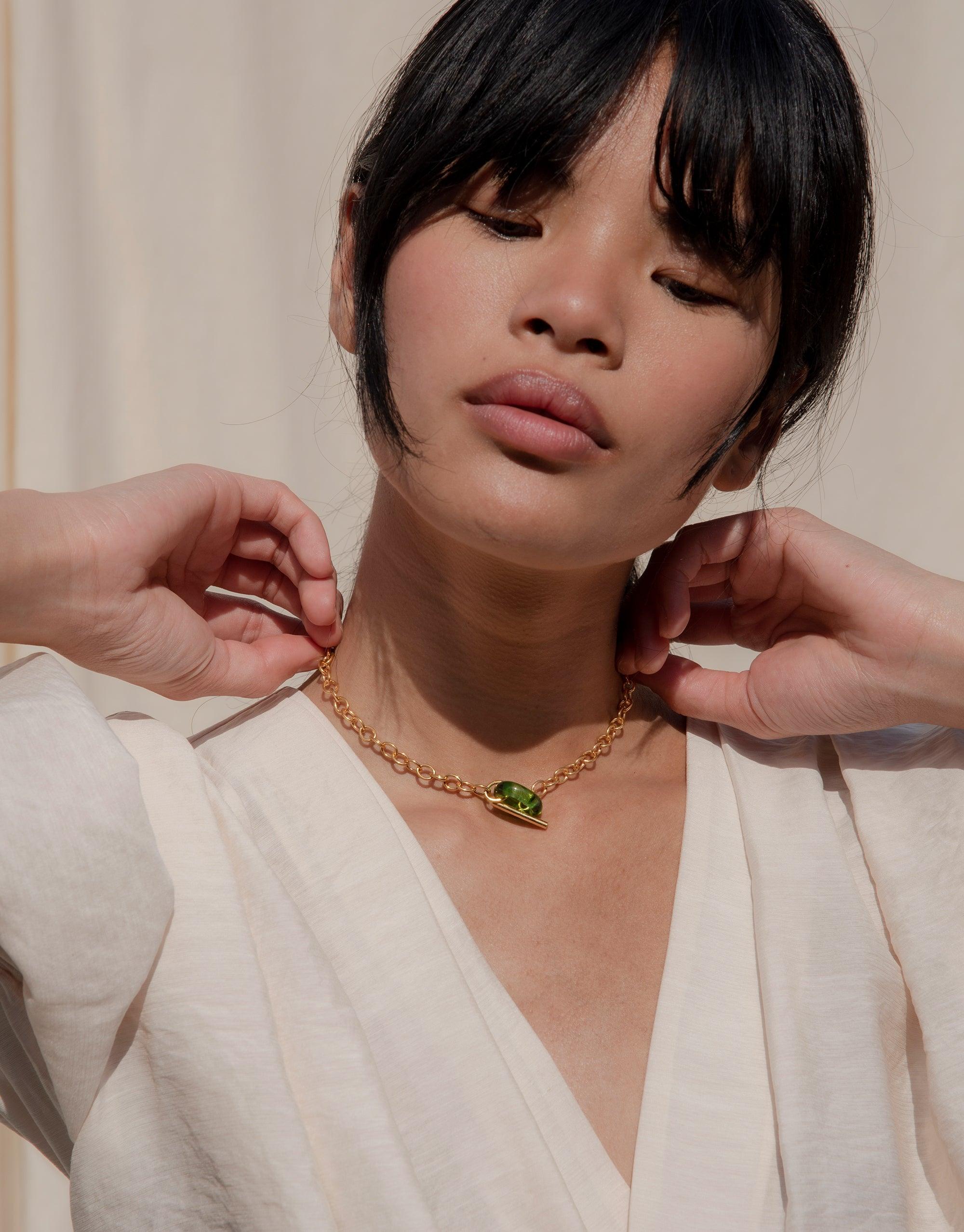 Elegant gold choker necklace with interlocking links and green eco gem pendant, worn by model in white top. Adjustable length for versatile styling. Handmade sustainable jewelry piece. ITL Toggle Choker Necklace by CLED
