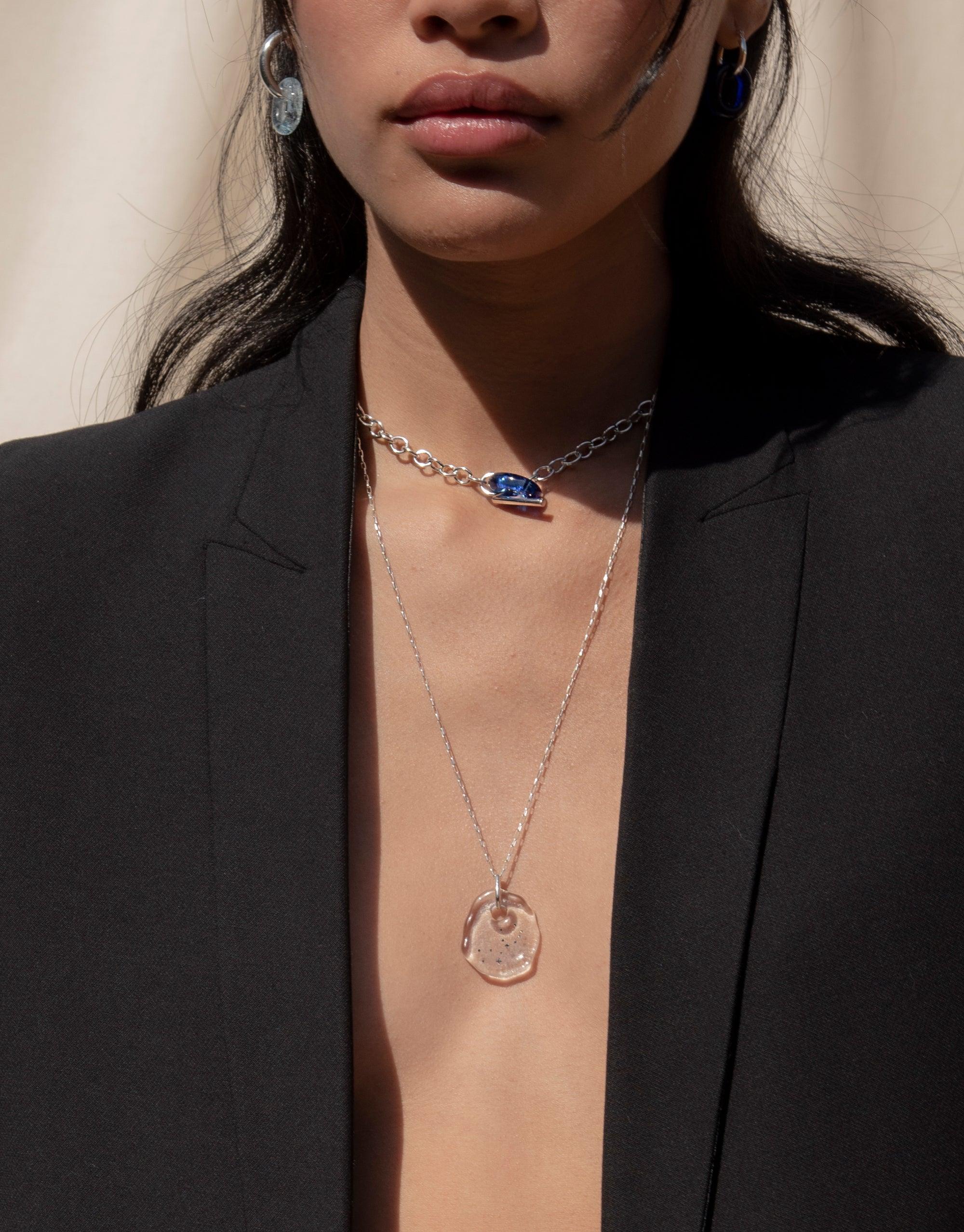 Elegant Constellation Necklace with circular glass pendant featuring engraved zodiac symbols, paired with a delicate silver chain. Worn by model in black blazer, showcasing the necklace's versatile and sophisticated design. Handcrafted eco-friendly jewelry by CLED.