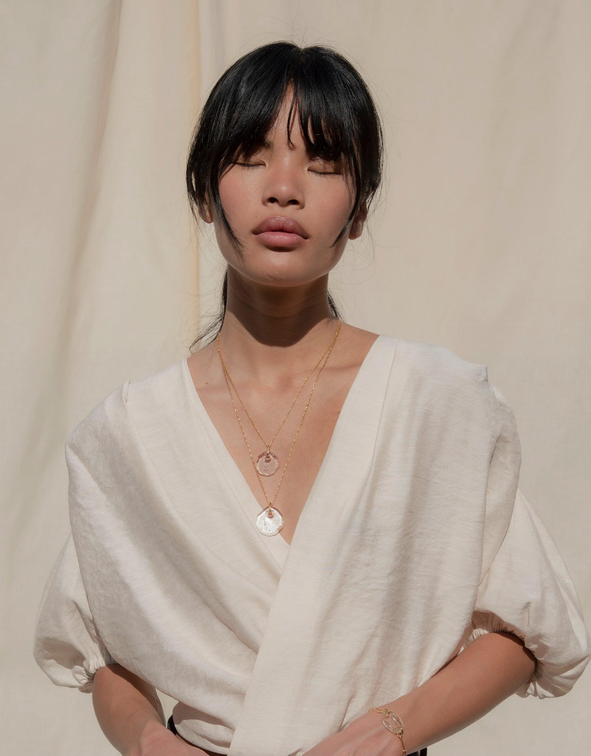 Elegant model wearing Messenger Necklace with Clear Engraving, featuring organic-shaped pendant on delicate chain. Soft, neutral background highlights sustainable eco gem jewelry. Stylish and personalized accessory for thoughtful communication. CLED Messenger Necklace | Clear Engraving