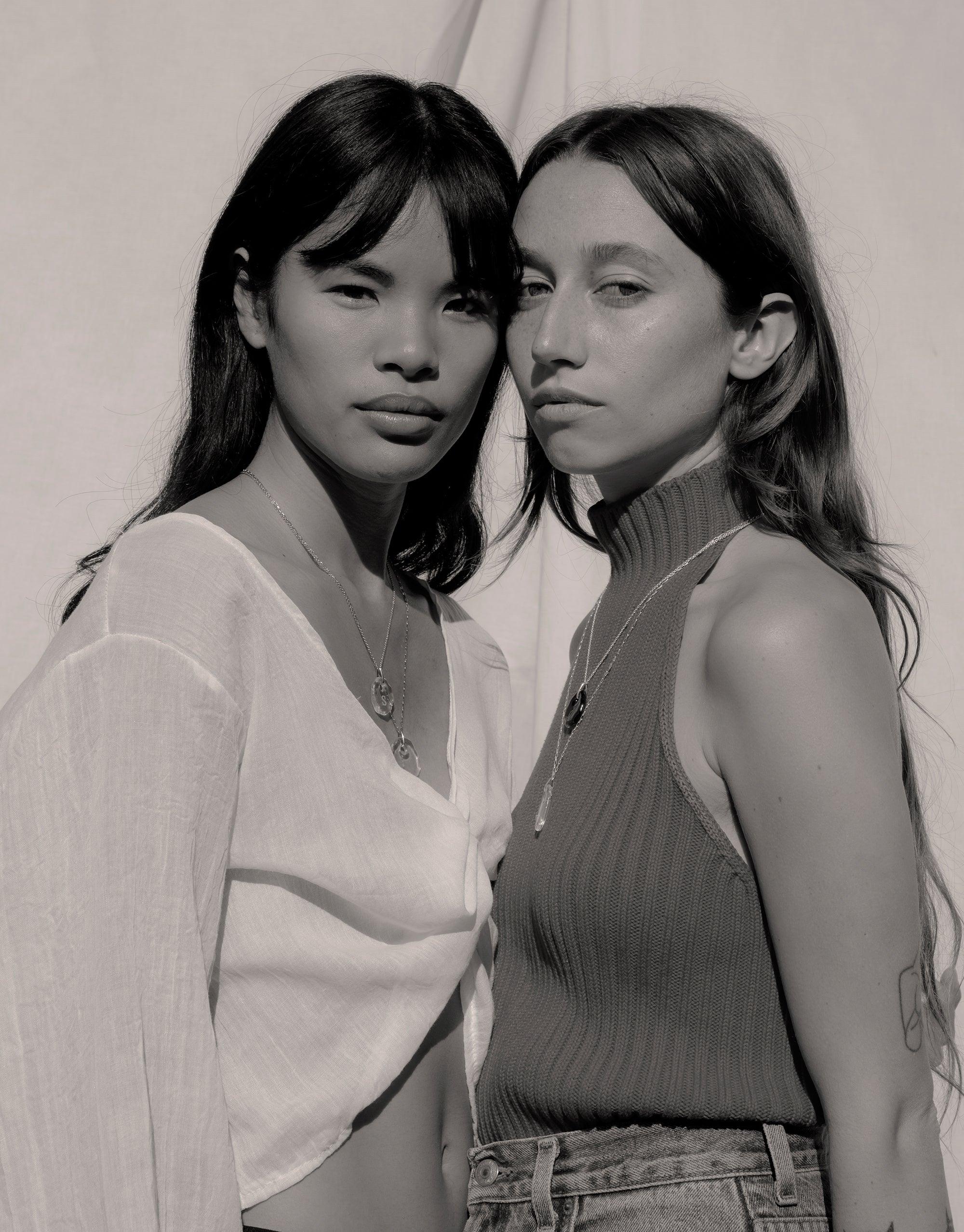 Two models wearing Constellation Necklaces from the Messenger Collection, showcasing delicate pendants on silver chains. Black and white image highlighting the necklaces' elegant design. Sustainable jewelry by CLED.