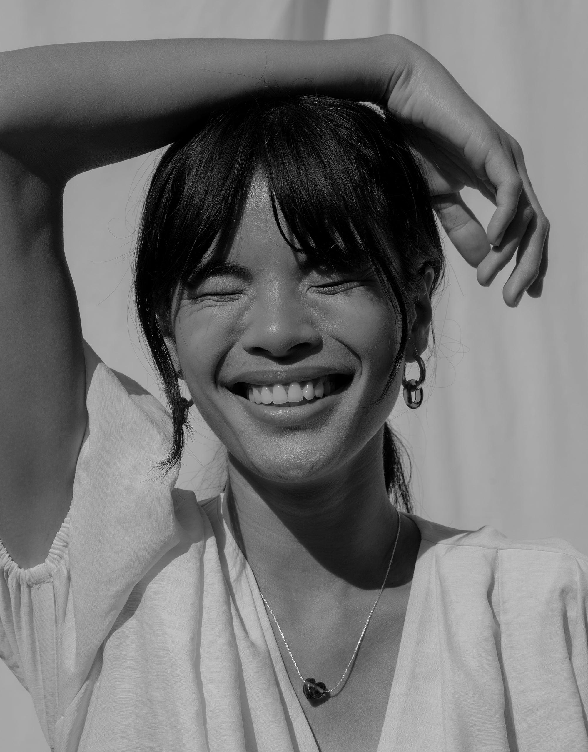 Black and white portrait of a person wearing large hoop earrings, smiling with eyes closed, hand raised. Showcasing In The Loop Hoops | Large, handcrafted eco-friendly jewelry by CLED.