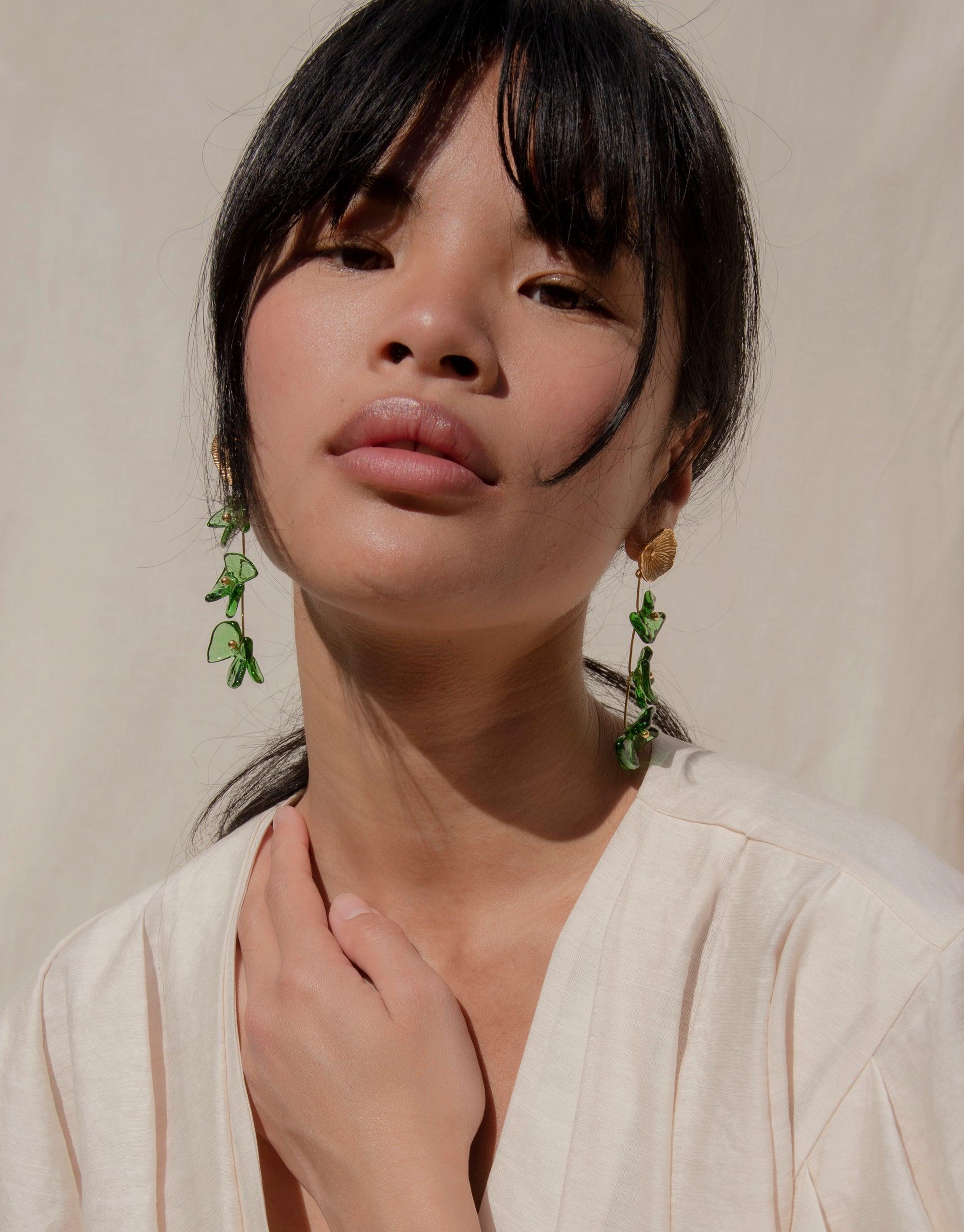Elegant model wearing Periwinkle Trio Earrings, showcasing delicate green glass petal drops against light background. Handcrafted eco-friendly jewelry with earthy charm. Sustainable fashion accessory by CLED, Periwinkle Trio Earrings.