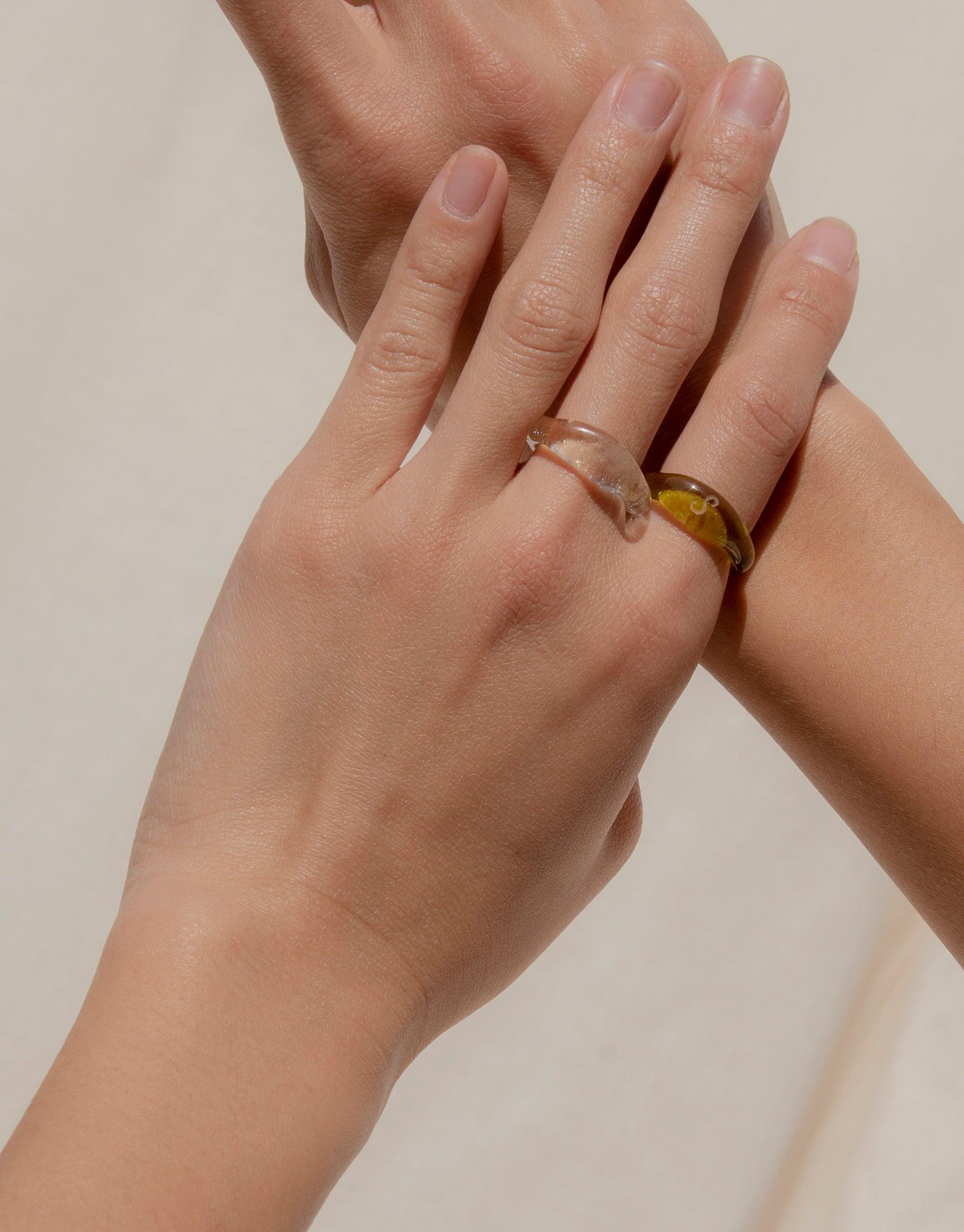 Close-up of hands wearing Engravable Signet Rings from the Messenger Collection, showcasing clear and yellow eco gem colors. Handcrafted, sustainable jewelry perfect for personalized messages and connection. Made in Los Angeles by CLED.