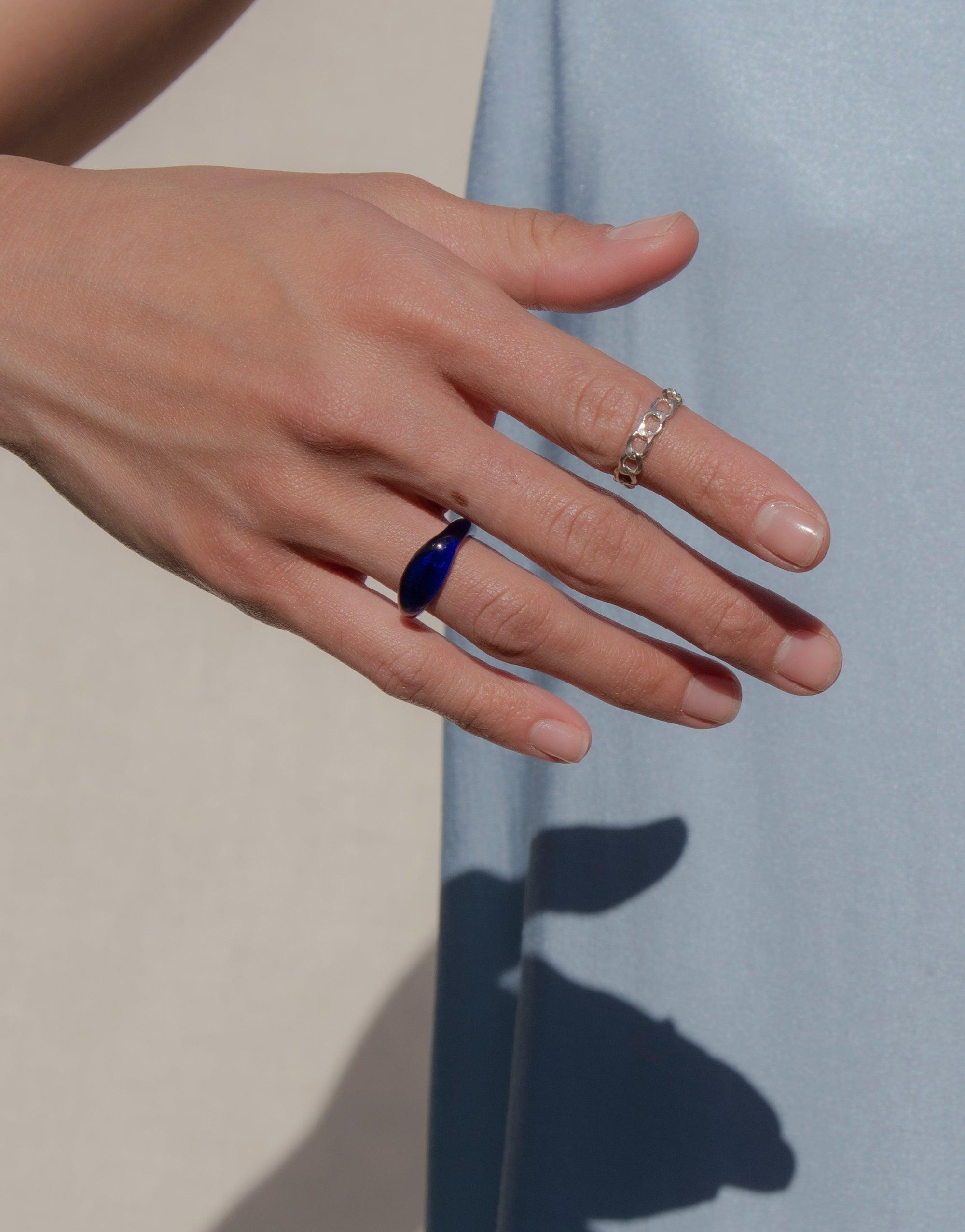 Close-up of a hand wearing an Engravable Signet Ring with a blue eco gem, showcasing the Messenger Collection's personalized design. The ring is paired with a delicate band, highlighting CLED's sustainable and stylish jewelry.