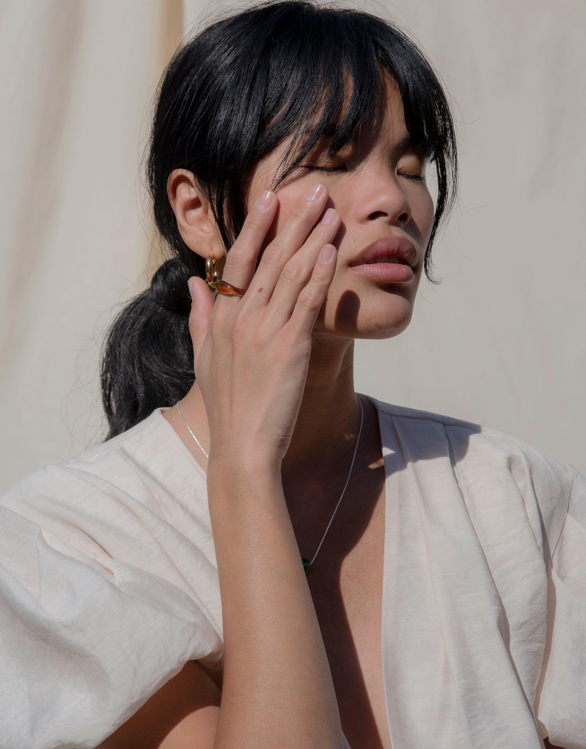 Person wearing Engravable Signet Ring from CLED's Messenger Collection, showcasing eco-friendly jewelry. Hand touching face to highlight ring, demonstrating elegant design and personalized etching. Sustainable fashion statement piece made in Los Angeles. CLED