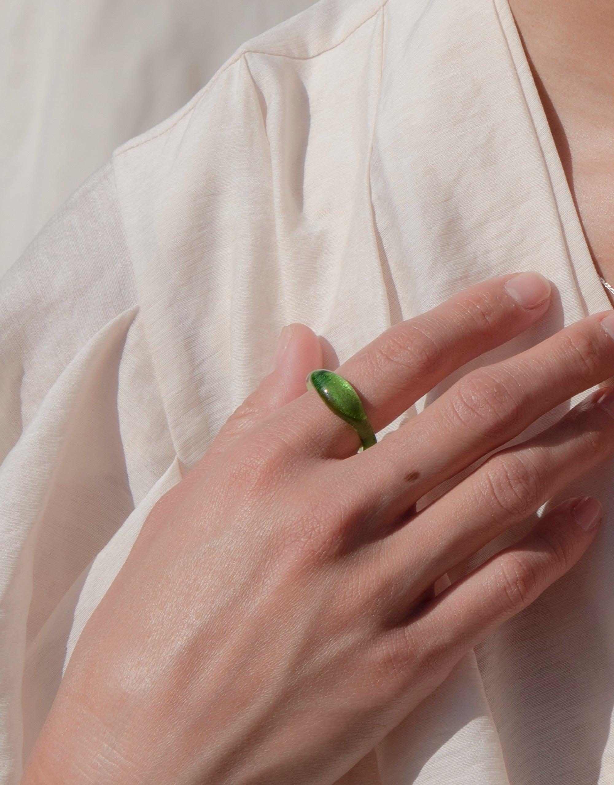 Close-up of hand wearing a green eco-friendly signet ring from the Messenger Collection, showcasing the Signet Ring Original by CLED. The ring features a vibrant, handcrafted eco gem made from repurposed glass, demonstrating sustainable jewelry design.