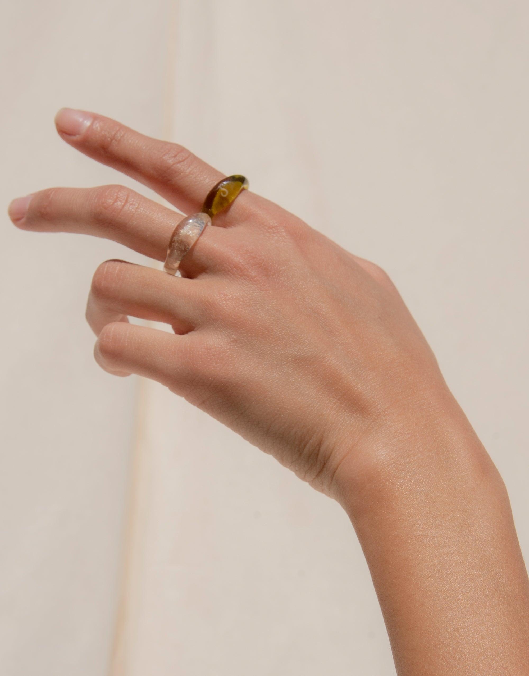 Hand wearing two Engravable Signet Rings from the Messenger Collection, showcasing eco-friendly glass designs in amber and clear colors. Sustainable, personalized jewelry for meaningful communication. CLED Engravable Signet Ring.