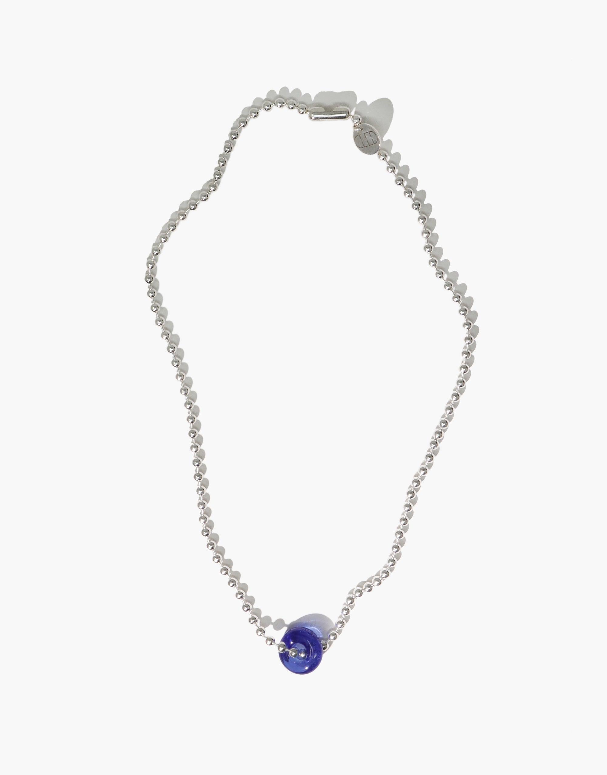 Elegant Donut Ball Necklace featuring a silver chain with a vibrant blue eco gem pendant, showcasing sustainable jewelry design. Handcrafted with repurposed glass, this necklace embodies eco-friendly luxury and prismatic beauty. CLED Donut Ball Necklace.