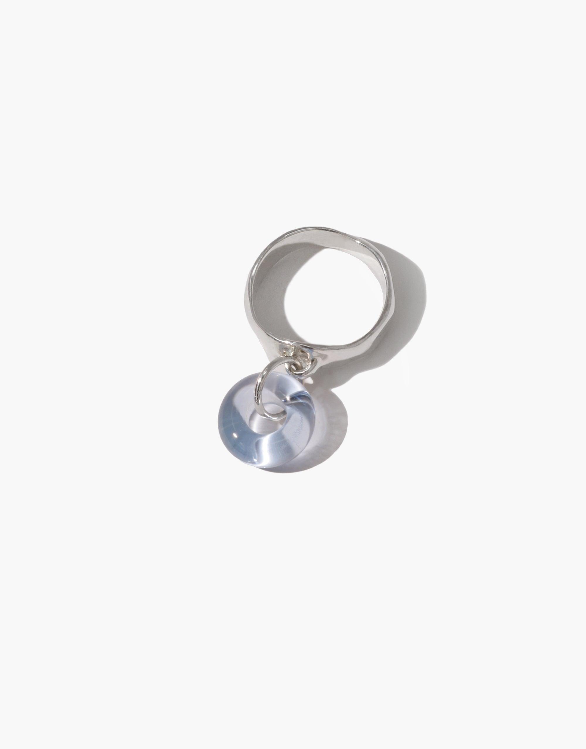 Donut Dangling Ring featuring a silver band with a transparent glass charm pendant. Unique eco-friendly jewelry made from upcycled glass bottles. Handcrafted design showcasing sustainable fashion and circular economy principles. CLED